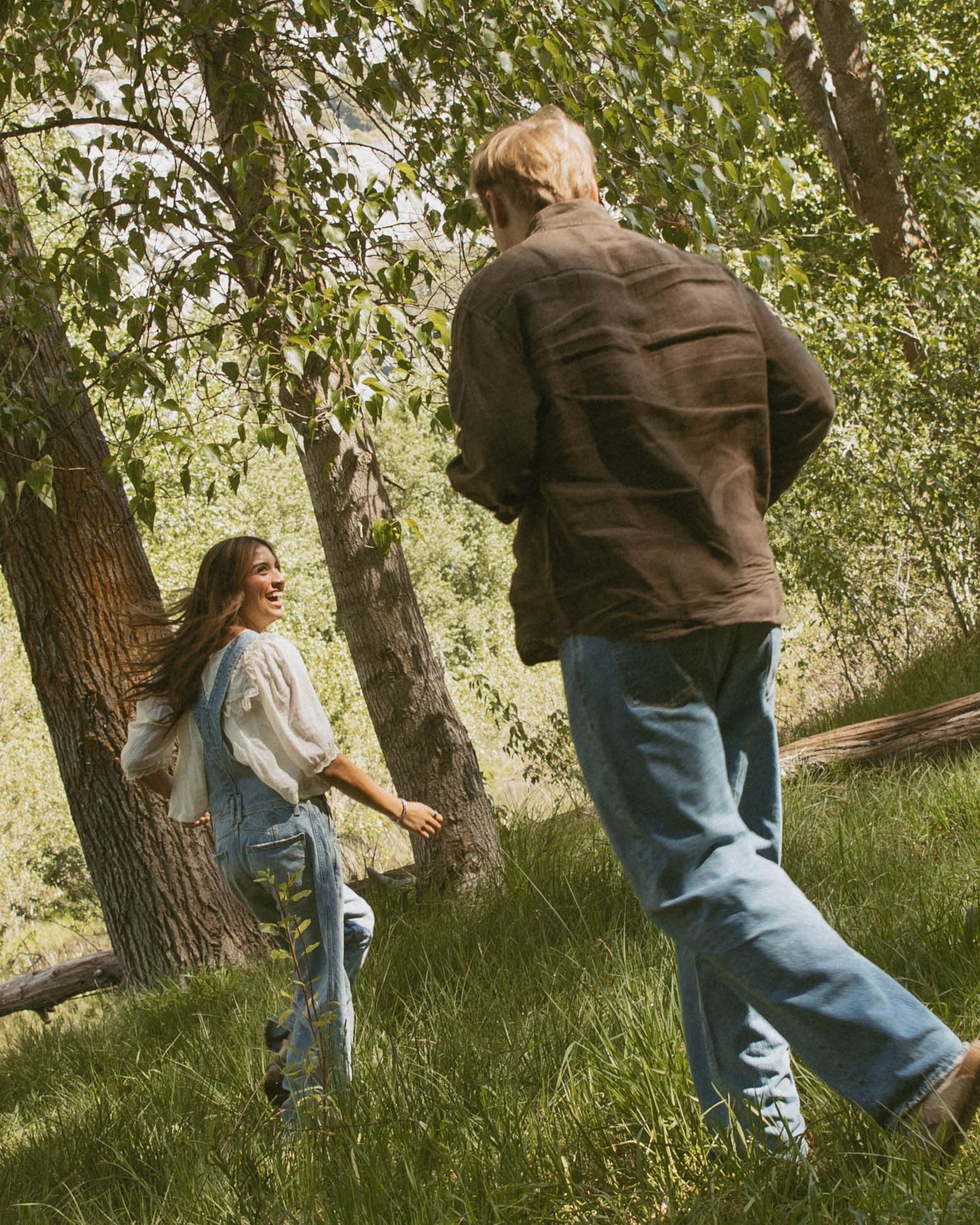 A man and woman walk together through a lush green forest, both wearing casual denim outfits.