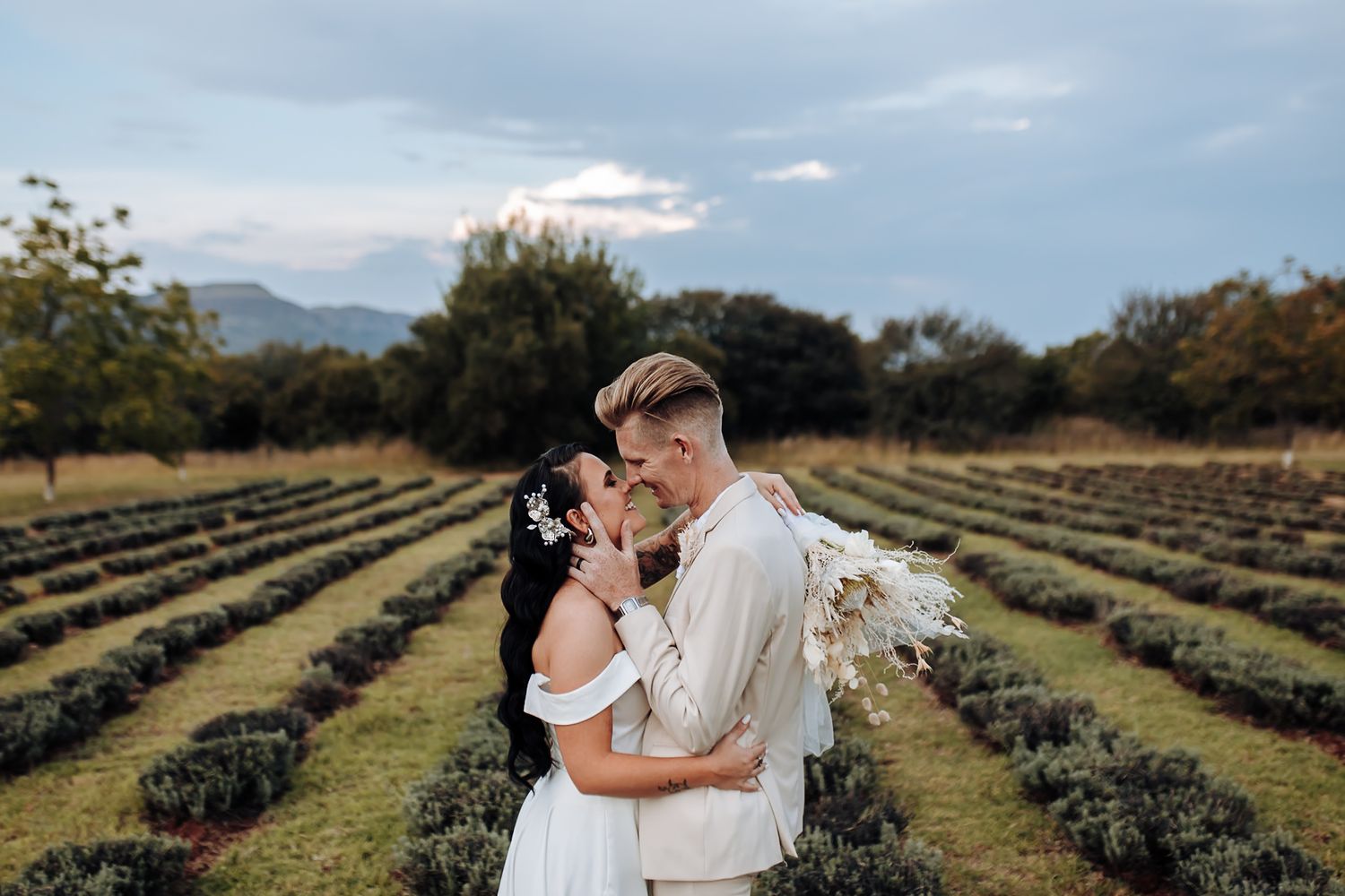 Couple shares tender moment together in lavender field on sunny day with mountains in background.