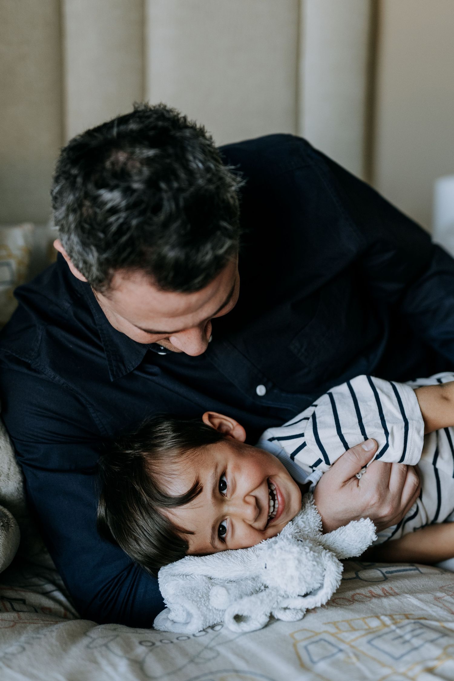 Parent and child cuddle with a soft white stuffed animal toy while relaxing on a bed.