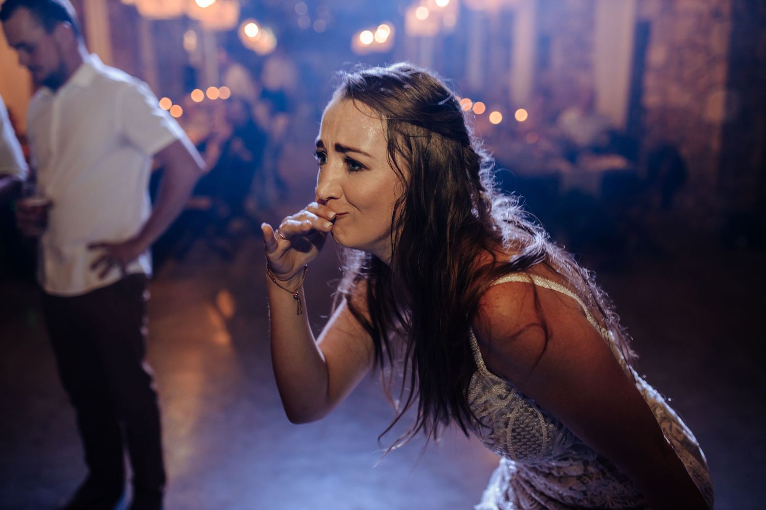 Person takes a drag from vape device in dimly lit nightclub with bokeh lighting effects in background.