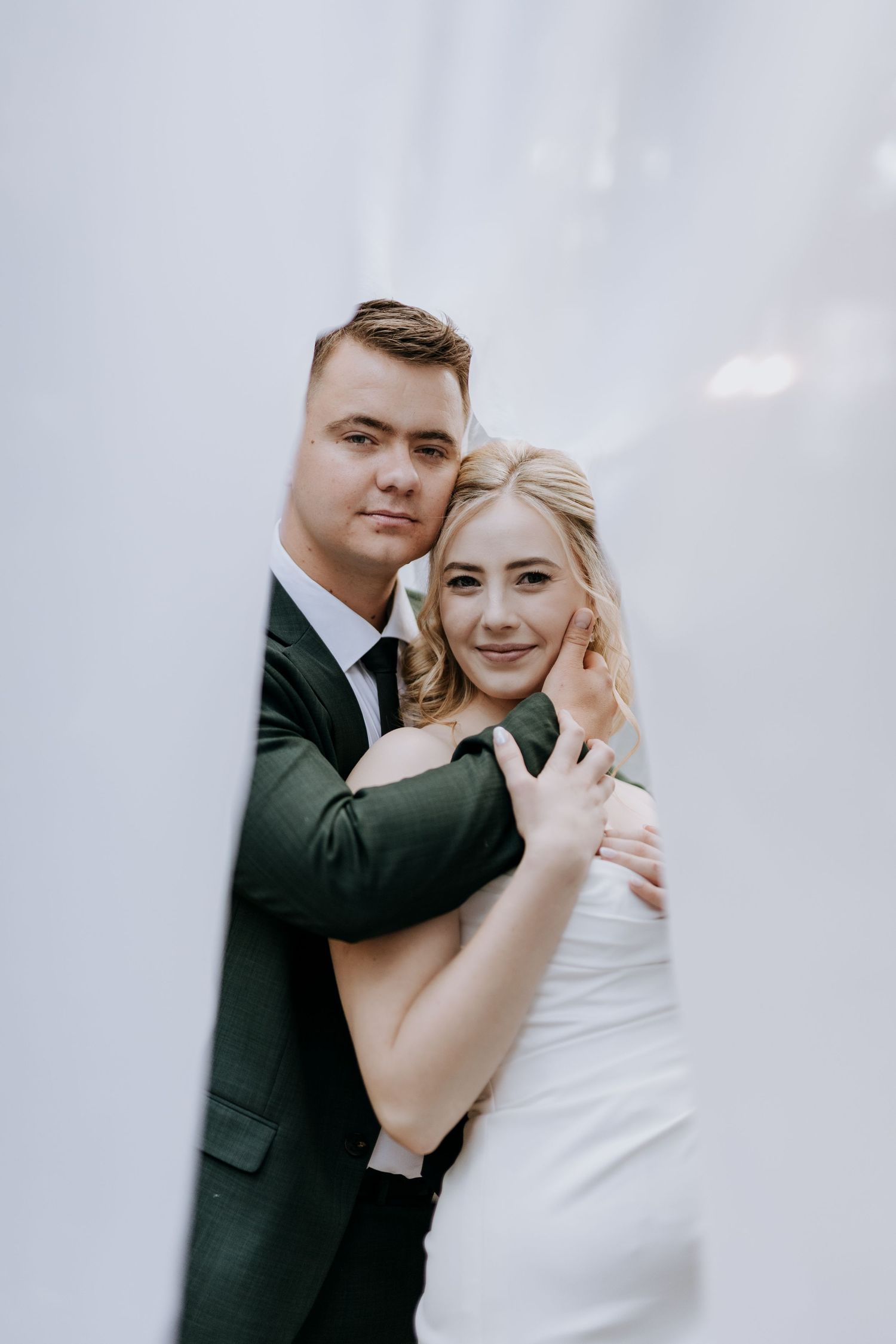 A couple in formal attire embracing during a romantic photoshoot with soft lighting and dreamy background.