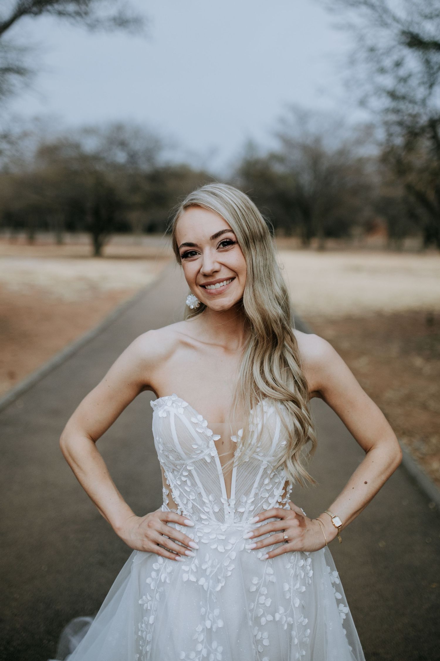 A bride in a white strapless wedding gown with lace details poses outdoors during a photo session.