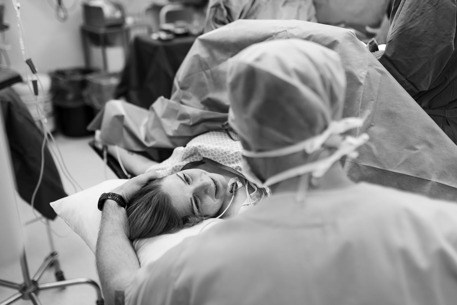 Black and white photo of a smiling woman in labor on a hospital bed surrounded by medical staff in scrubs.
