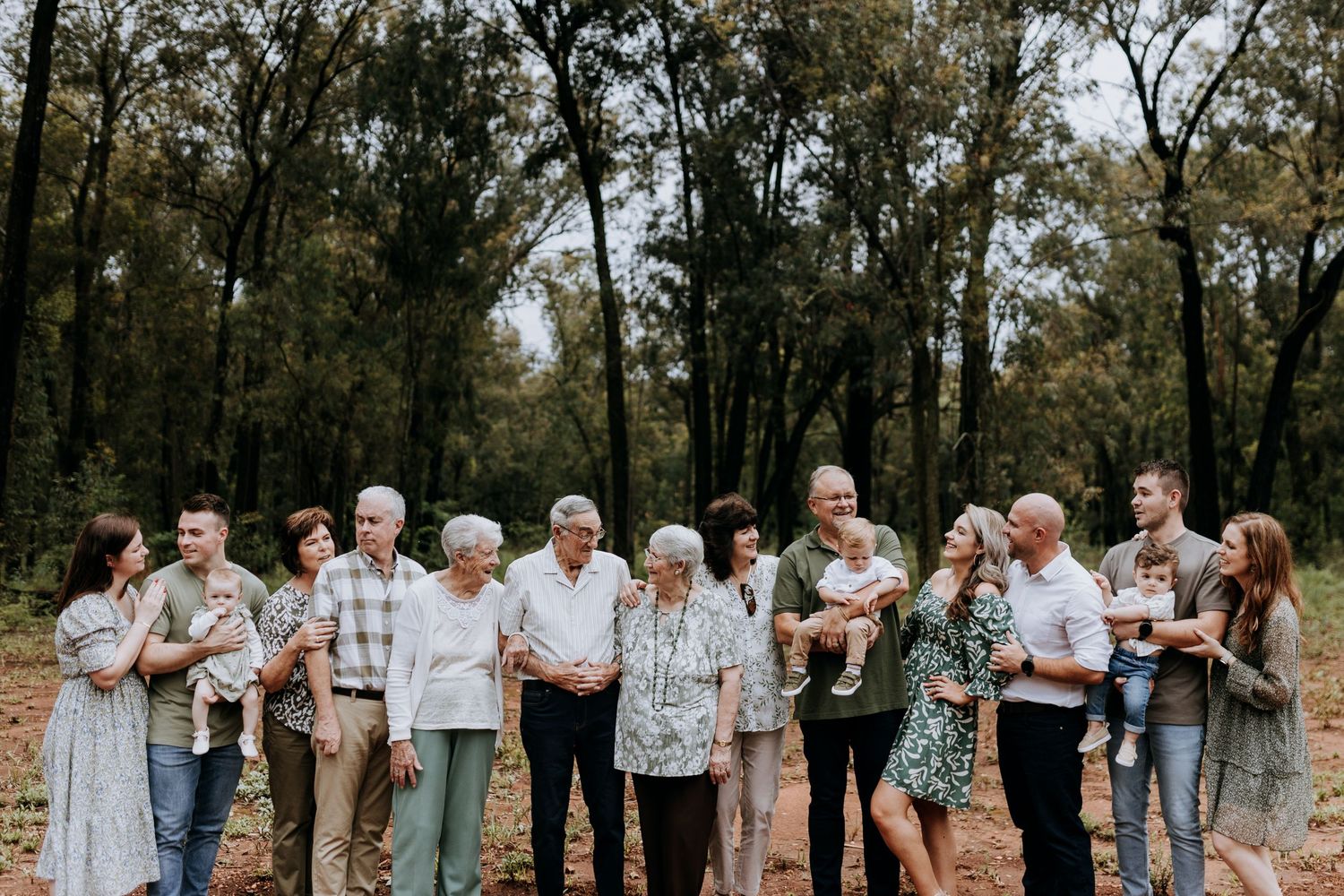 Family and friends pose for portrait photos in casual clothing while standing against a wooded backdrop.