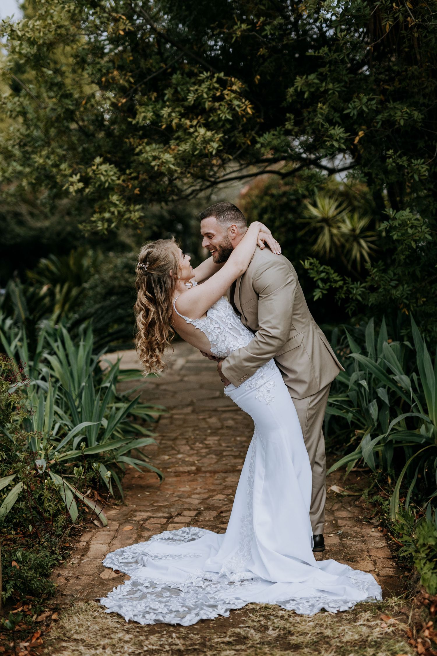 Wedding couple shares intimate dance pose on a garden path surrounded by lush tropical plants.