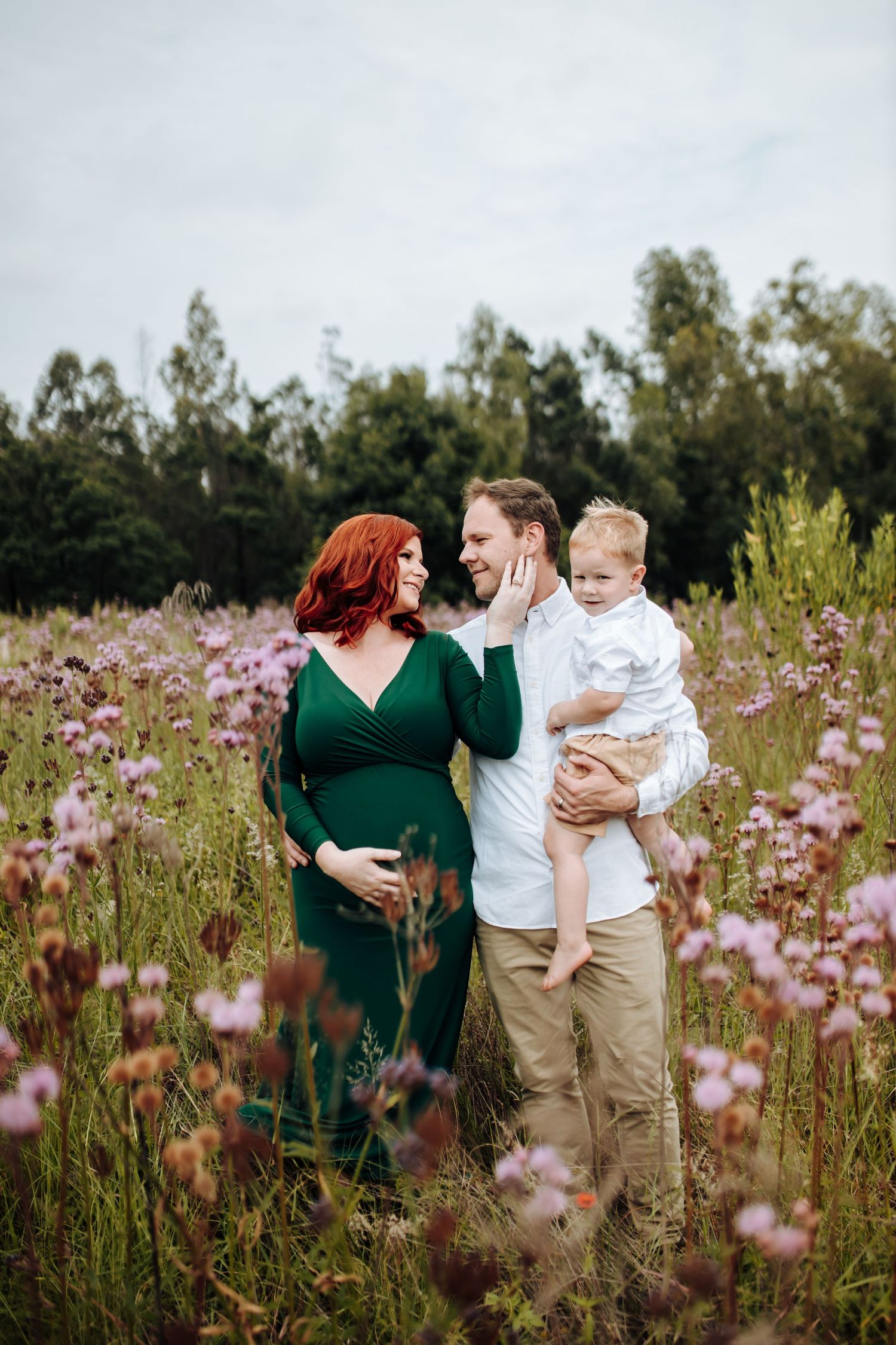 A family shares tender moments together in a blooming field of purple wildflowers during a golden hour photo session.