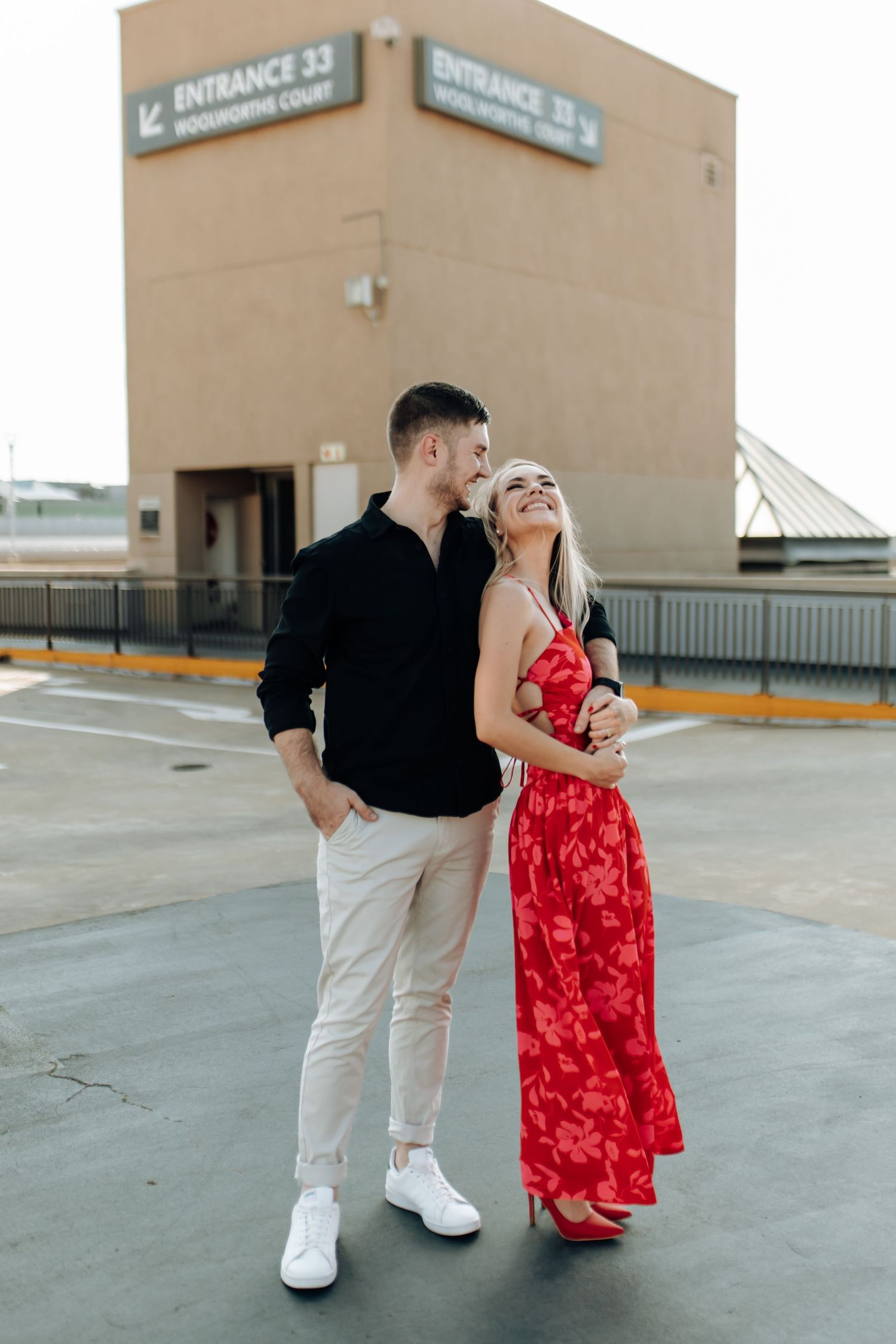 A couple in a parking lot wearing black and white with her in a striking red dress share an intimate moment.