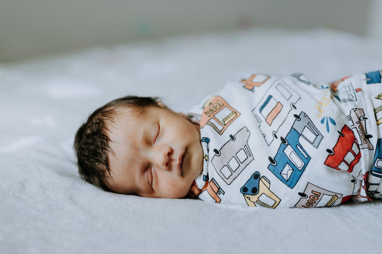 A sleeping baby wrapped in a cozy blanket with car print pattern.