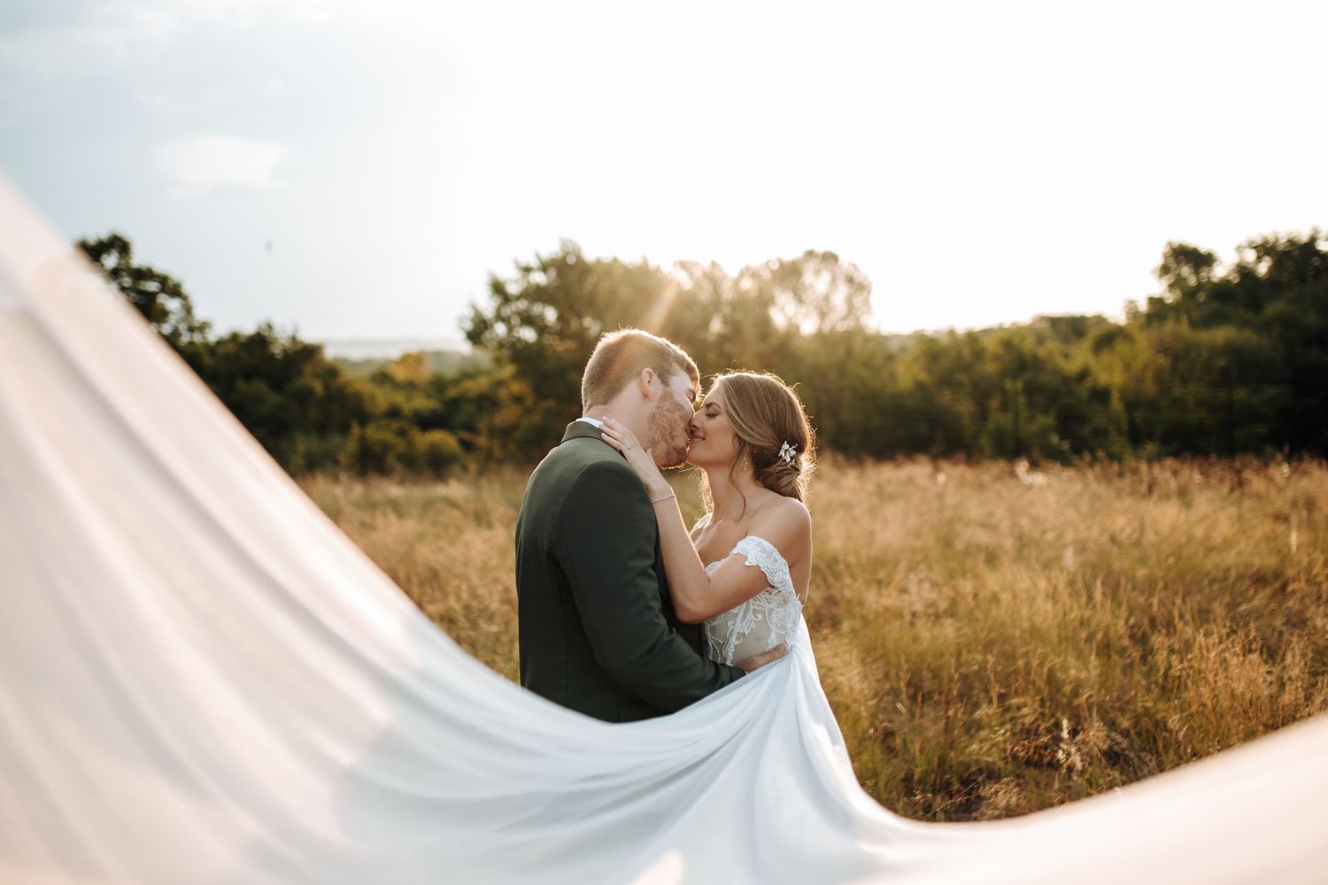 A gorgeous golden hour wedding photoshoot in a rustic field with wispy white veil flowing in the breeze.