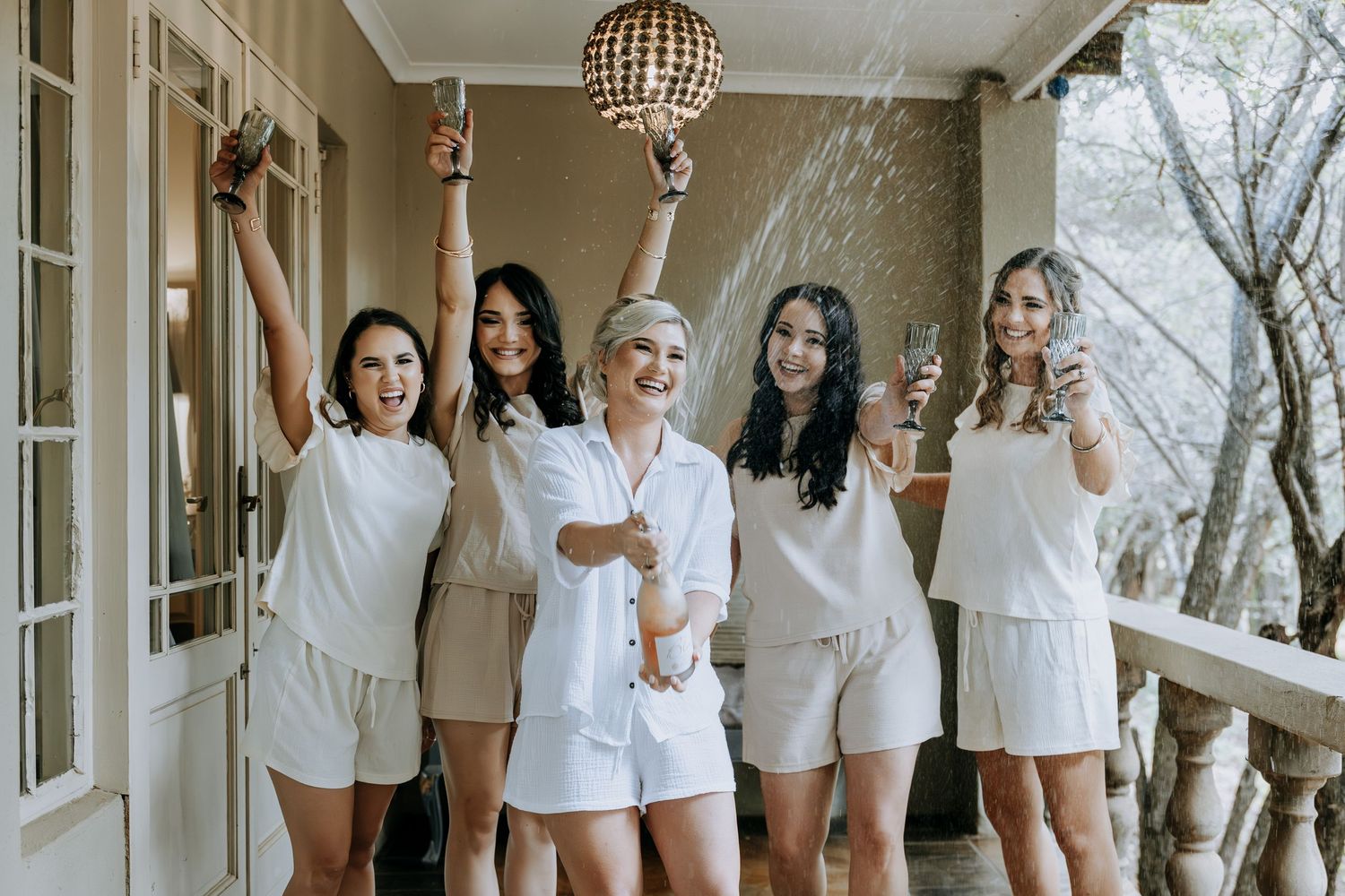 Group wearing matching white outfits poses together on a bright porch with natural light streaming through windows.