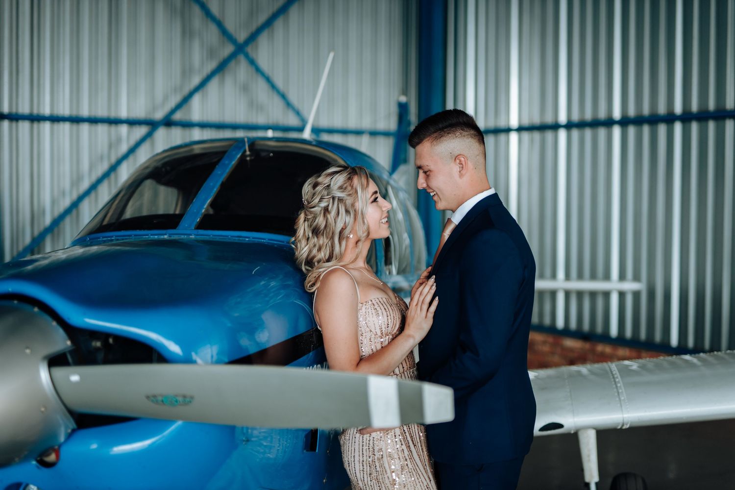 Couple poses romantically in an airplane hangar with a small aircraft in the background.