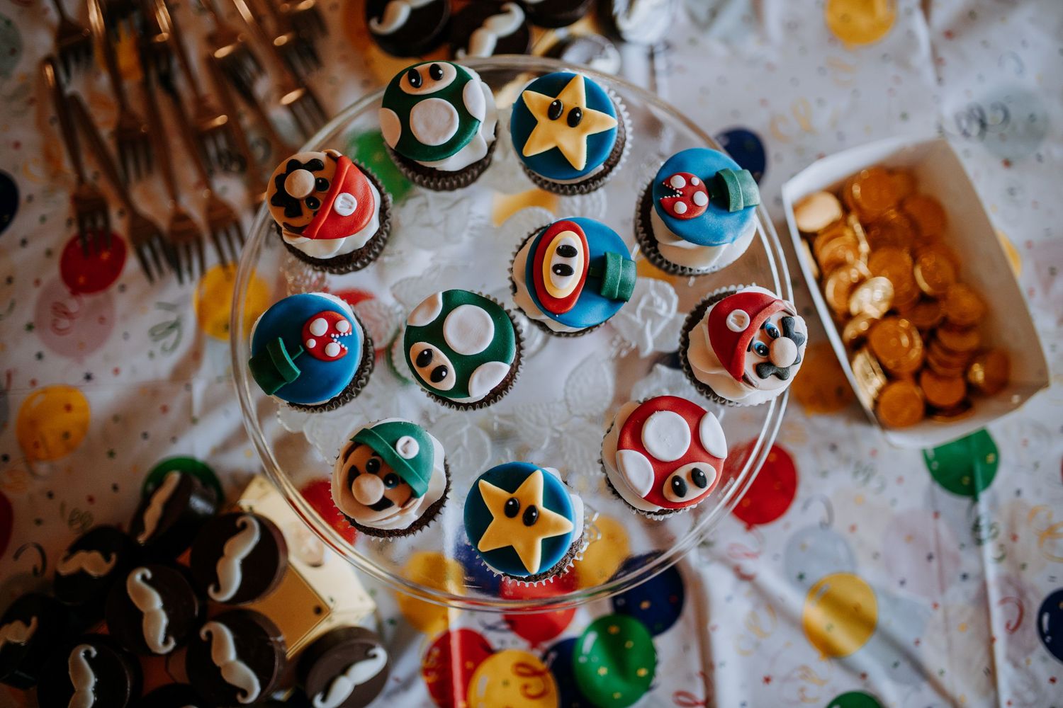 Colorful Super Mario-themed cupcake decorations with mushrooms, stars, and gaming icons arranged on a table.