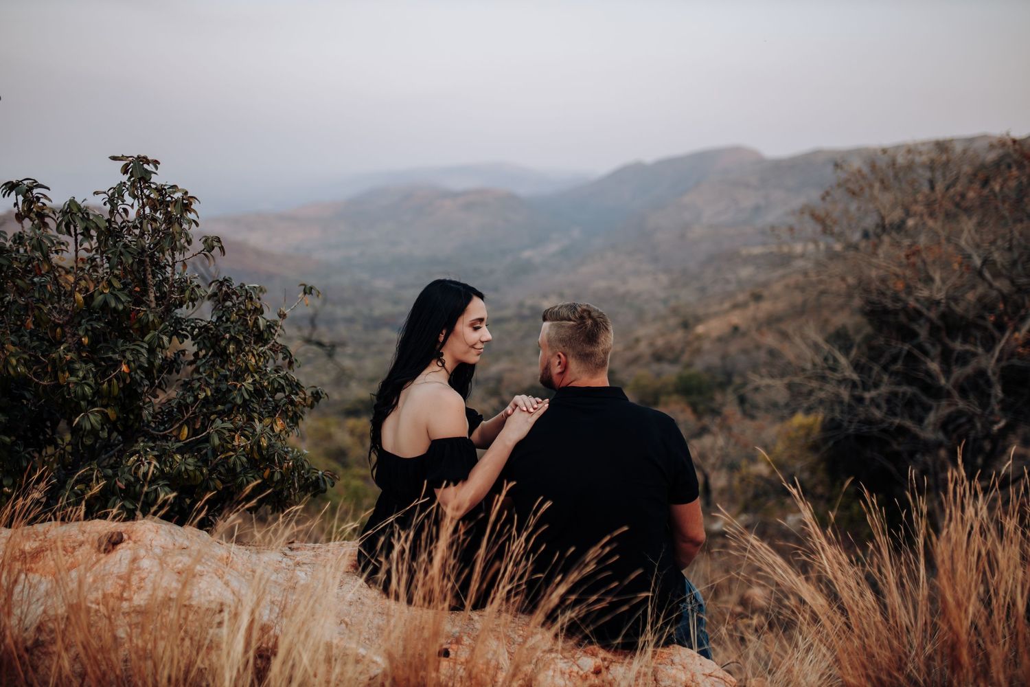 Scenic mountain landscape viewpoint with two individuals sharing an intimate moment at sunset in warm autumn lighting.