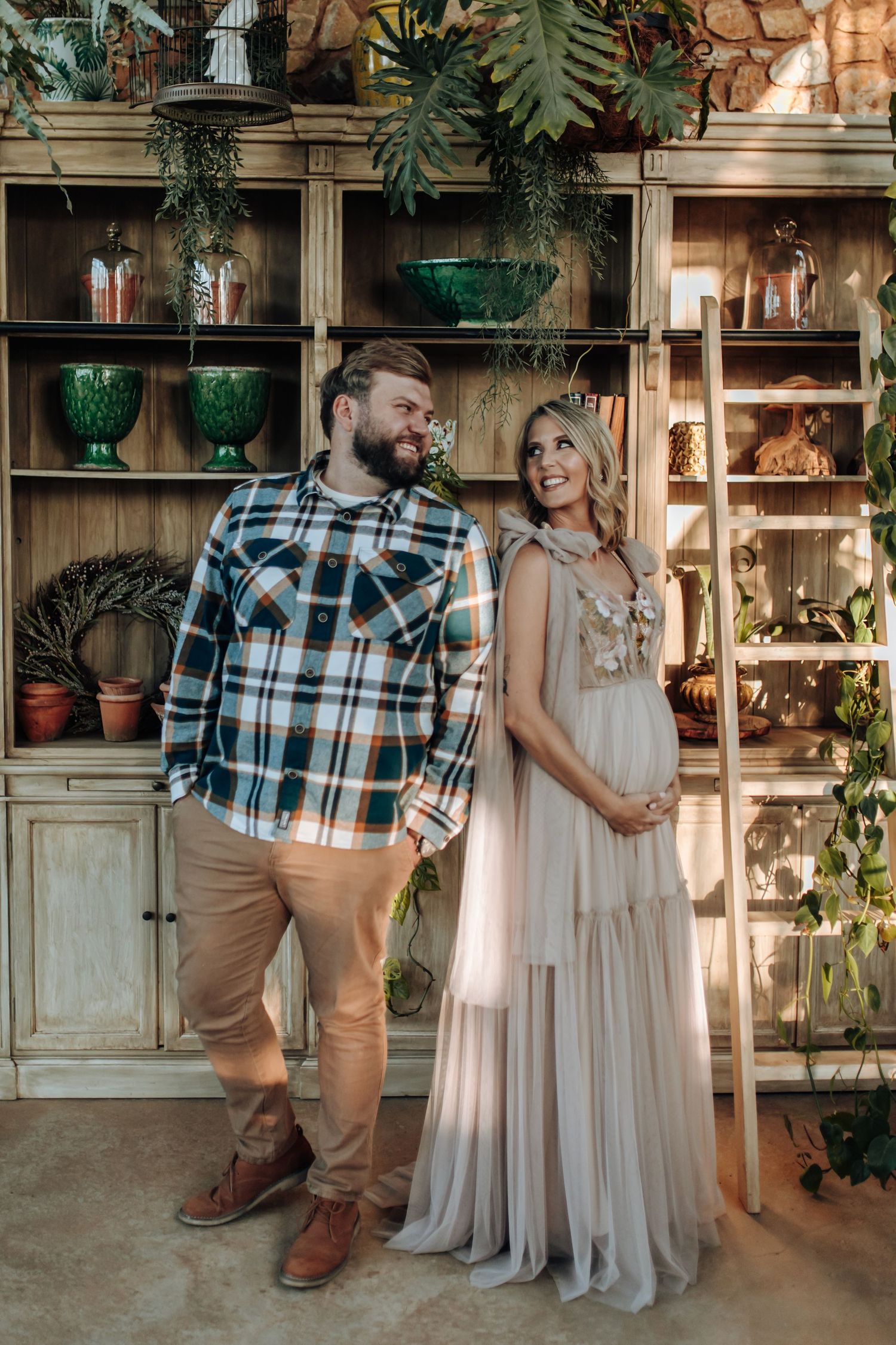 A couple shares tender moments in a rustic indoor setting with vintage furniture and plants in the background.
