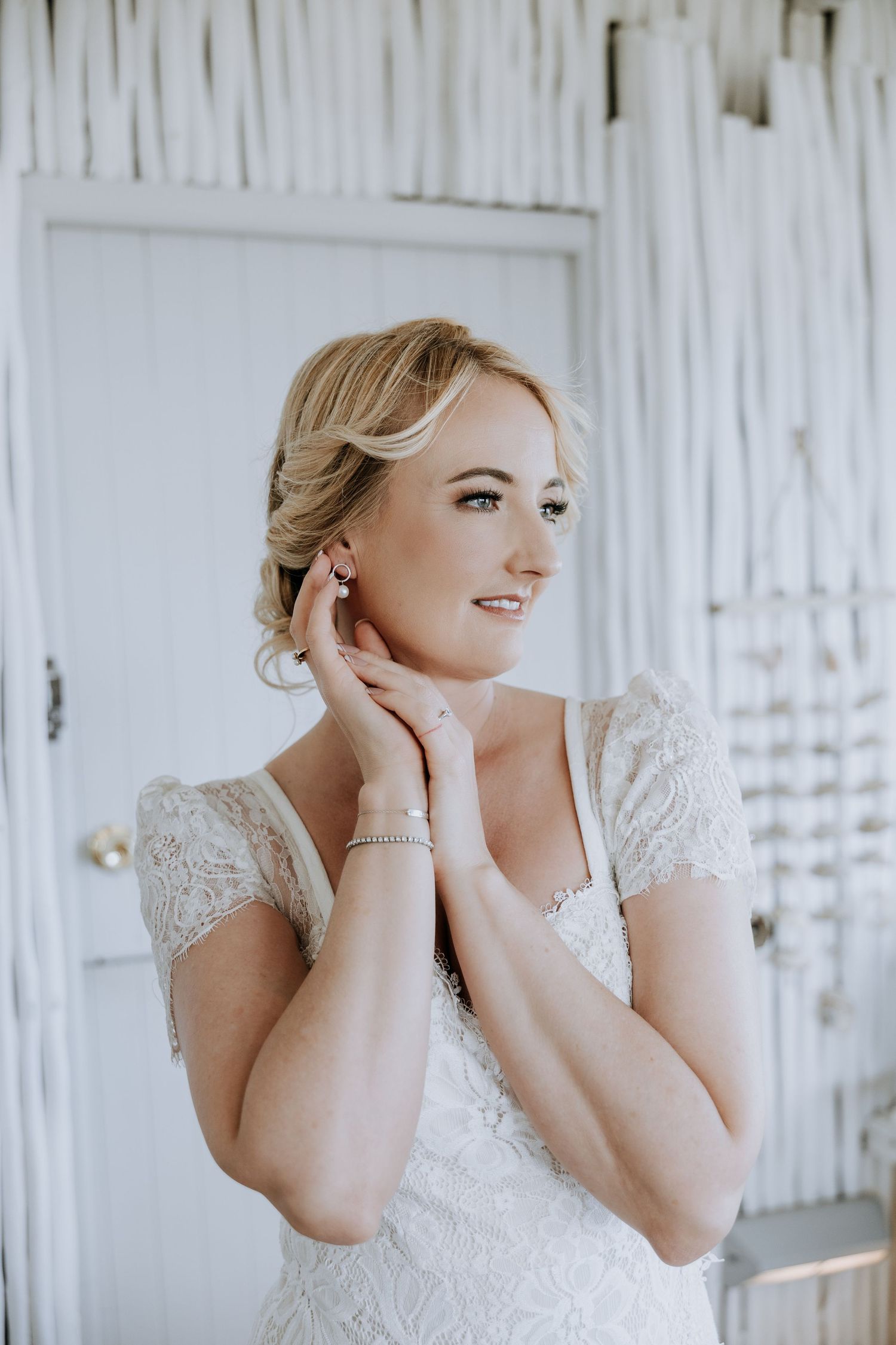A woman in a white lace wedding dress poses with elegant gestures against a white background.