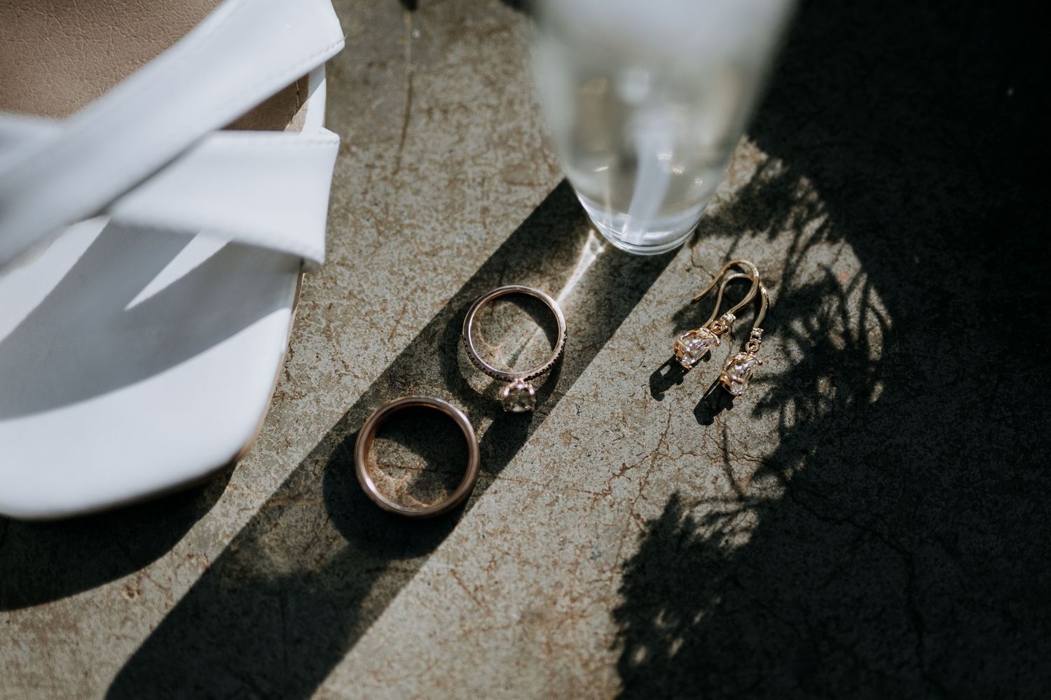 Wedding rings cast dramatic shadows on a textured stone surface beside white tableware in natural lighting.
