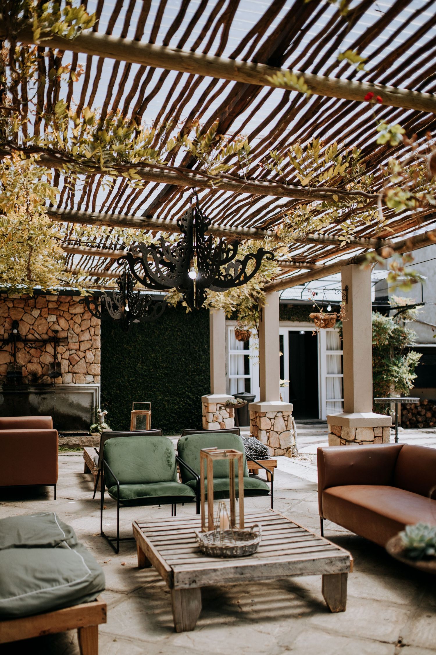 Rustic outdoor patio space with wooden pergola, stone walls, comfortable seating, and modern lighting fixtures creates a cozy ambiance.