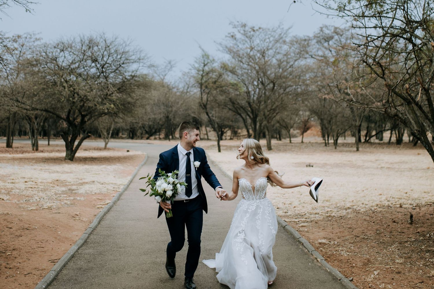 A couple walks hand in hand through a serene winter orchard with bare trees creating a romantic atmosphere.