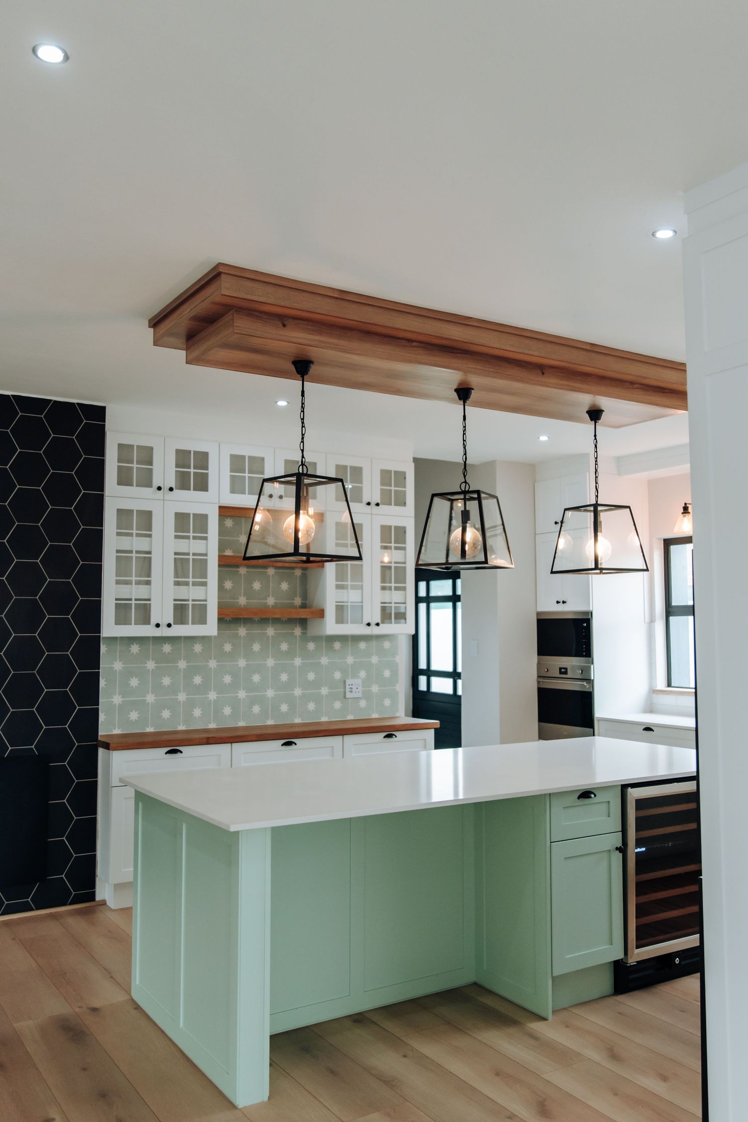 Modern kitchen with mint green island, white cabinets, geometric tile backsplash, and warm wood accents flows into open space.