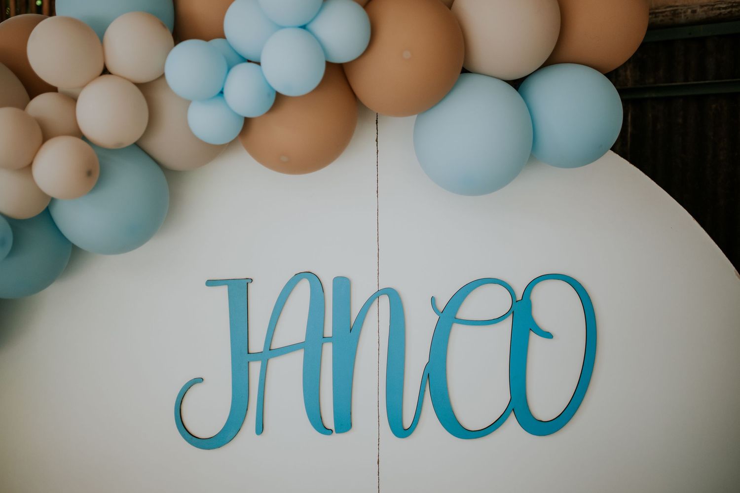 Baby shower celebration setup with blue and brown balloon arch decorations against a white wall.