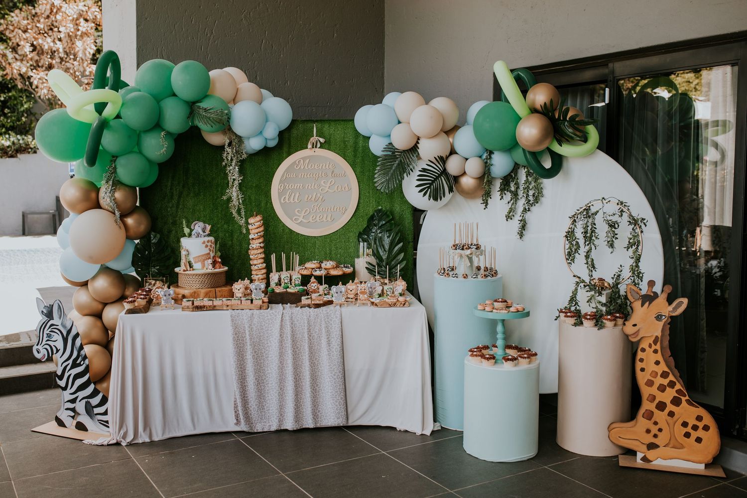 Safari themed baby shower room decorated with balloon garlands, stuffed animals, and pastel mint and peach colors.