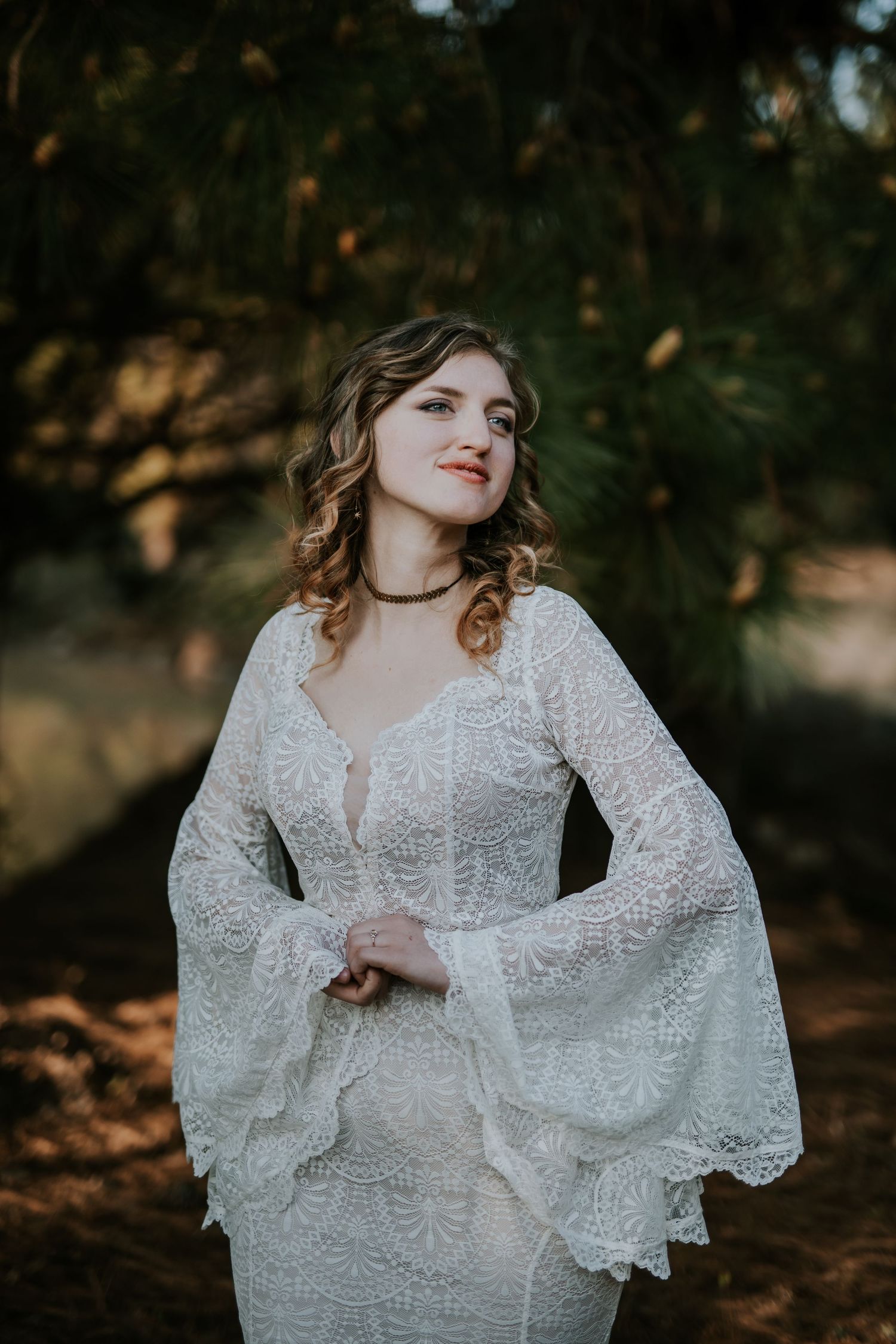 A romantic bridal portrait series with a lace bell sleeve wedding dress against a moody forest backdrop in autumn light.