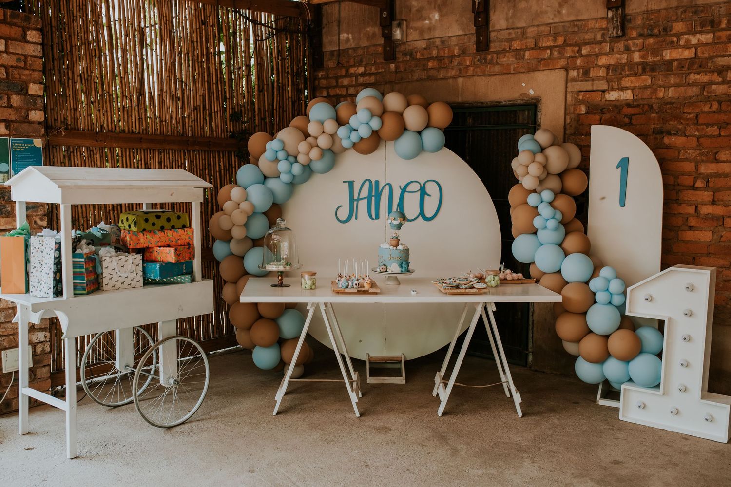 Modern baby shower or gender reveal party decorated with blue and white balloons and brick wall backdrop.