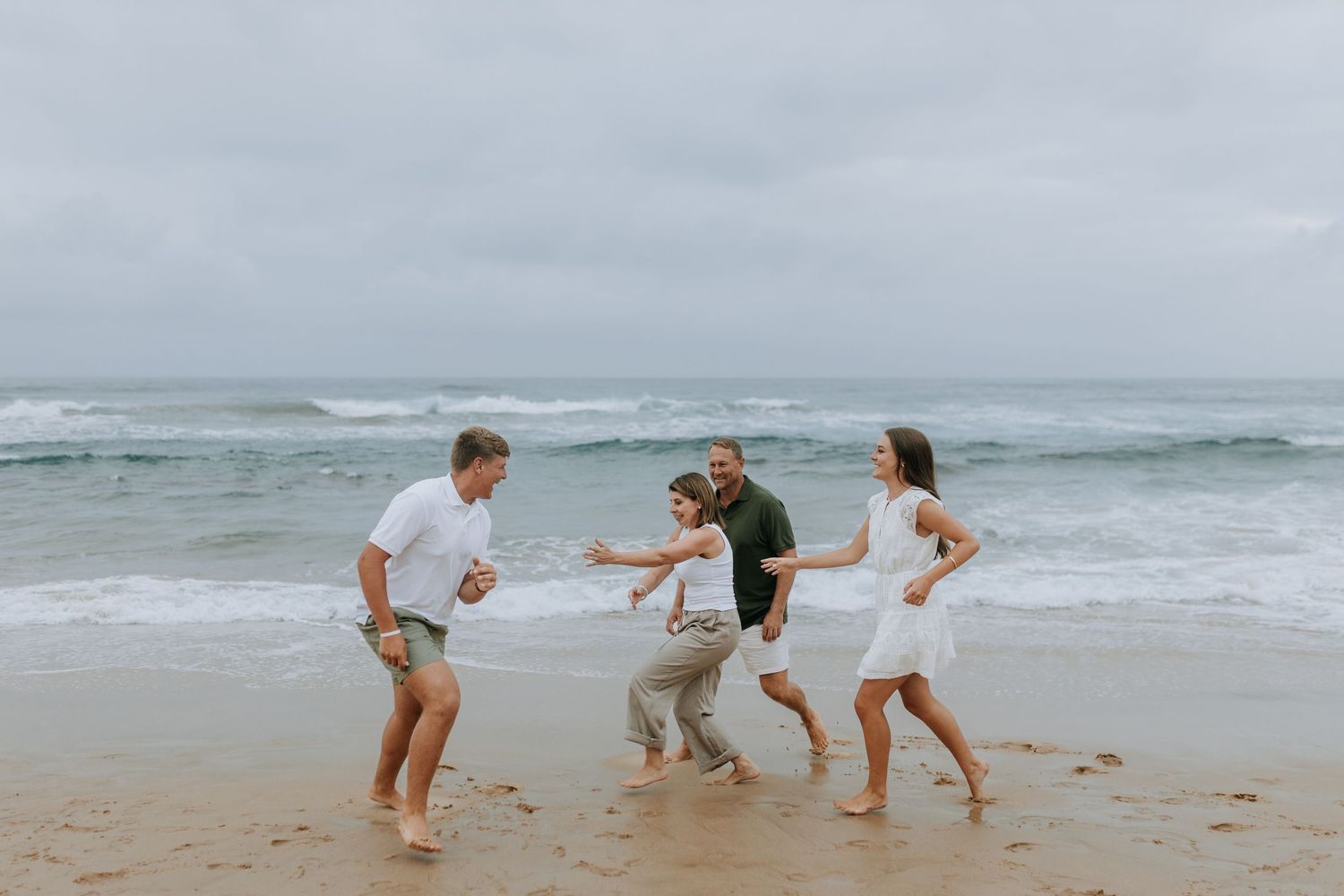 People playing and running on a rocky beach near the ocean during an overcast day.