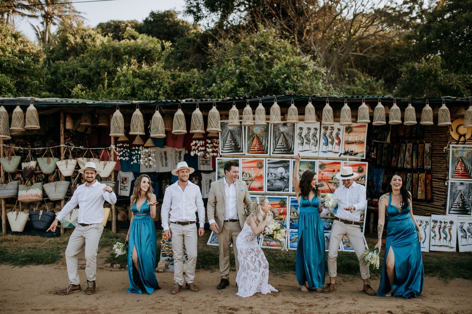 Wedding party members in white and turquoise attire walk together against a white picket fence backdrop.