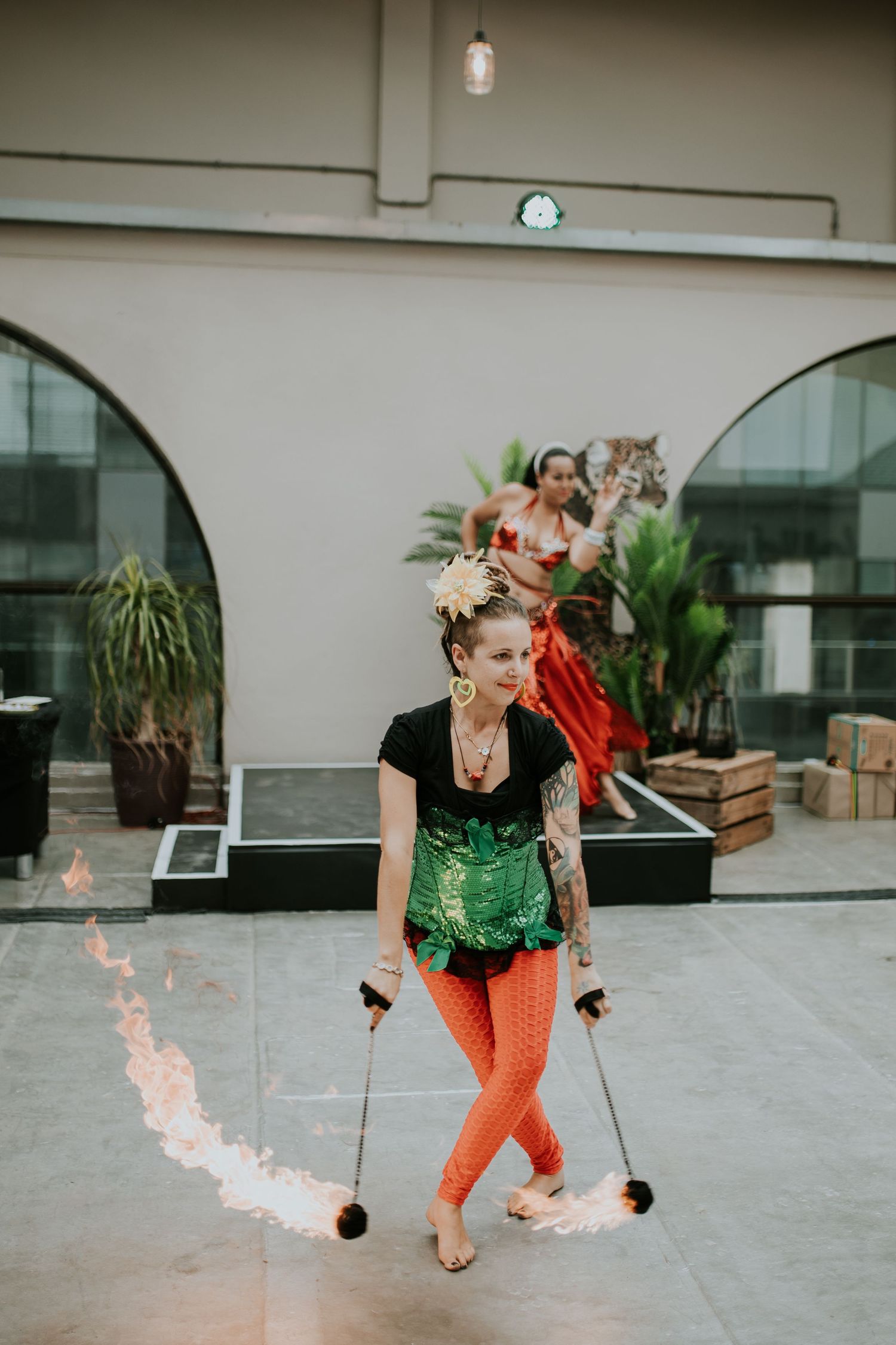 Performer in orange pants and green top spins fire props across a series of photos showing the fluid motion sequence.