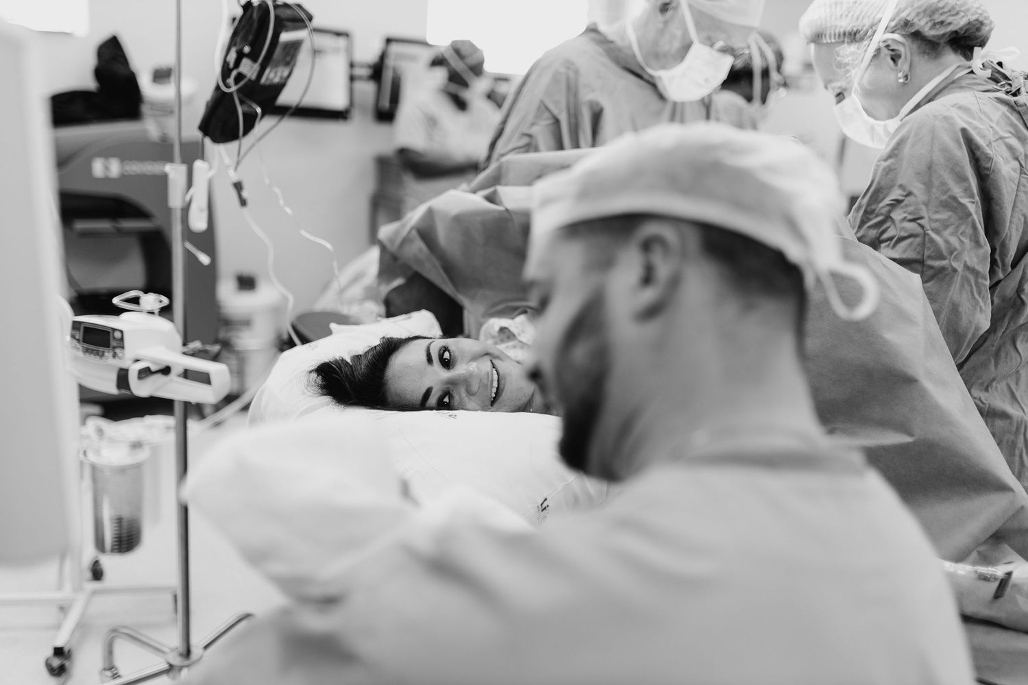 Black and white photo of a woman in labor with a supportive partner beside her in a hospital operating room.