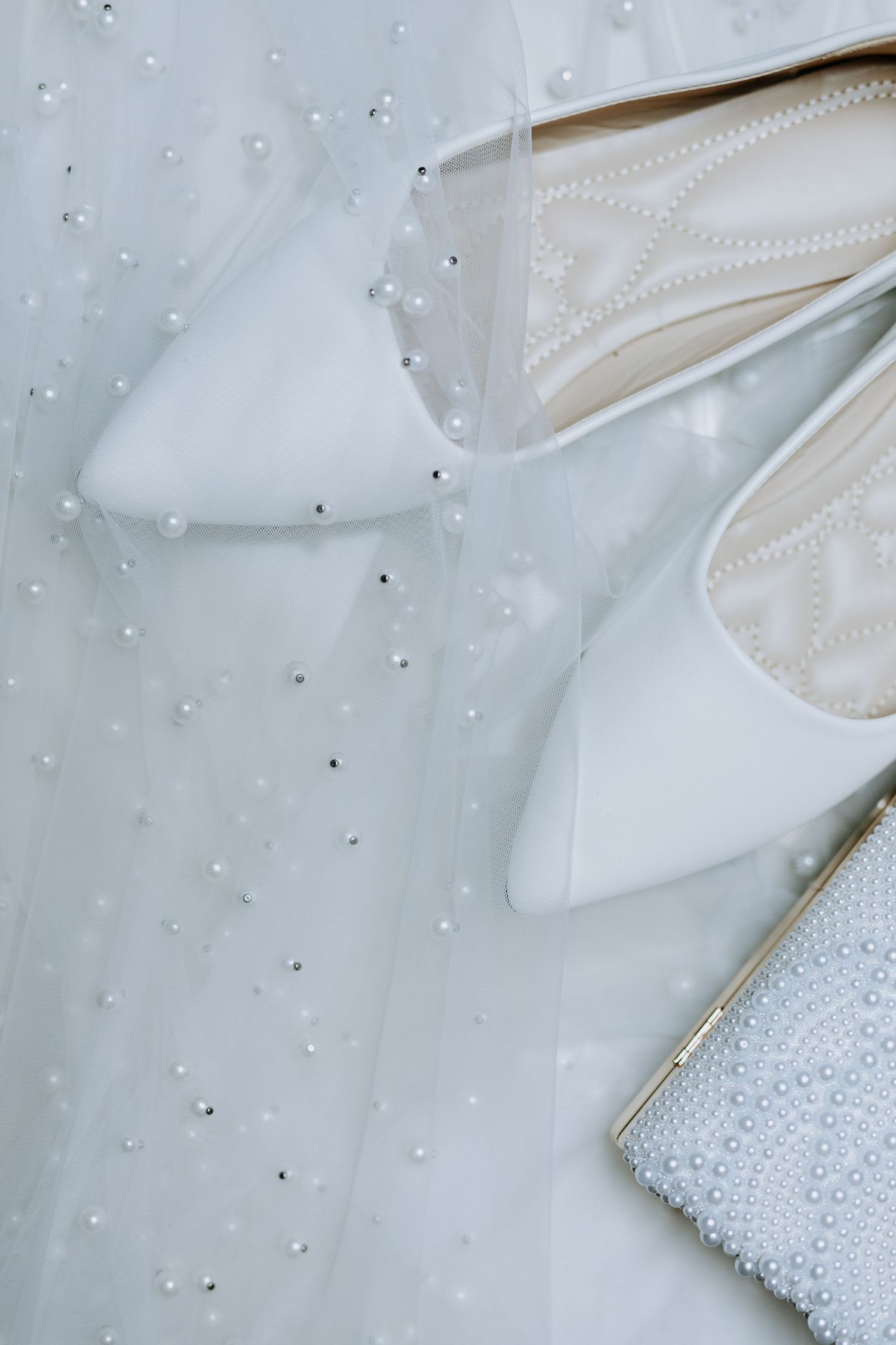 Close-up of white wedding dress fabric with delicate pearl beading and sparkly embellishments on a light background.