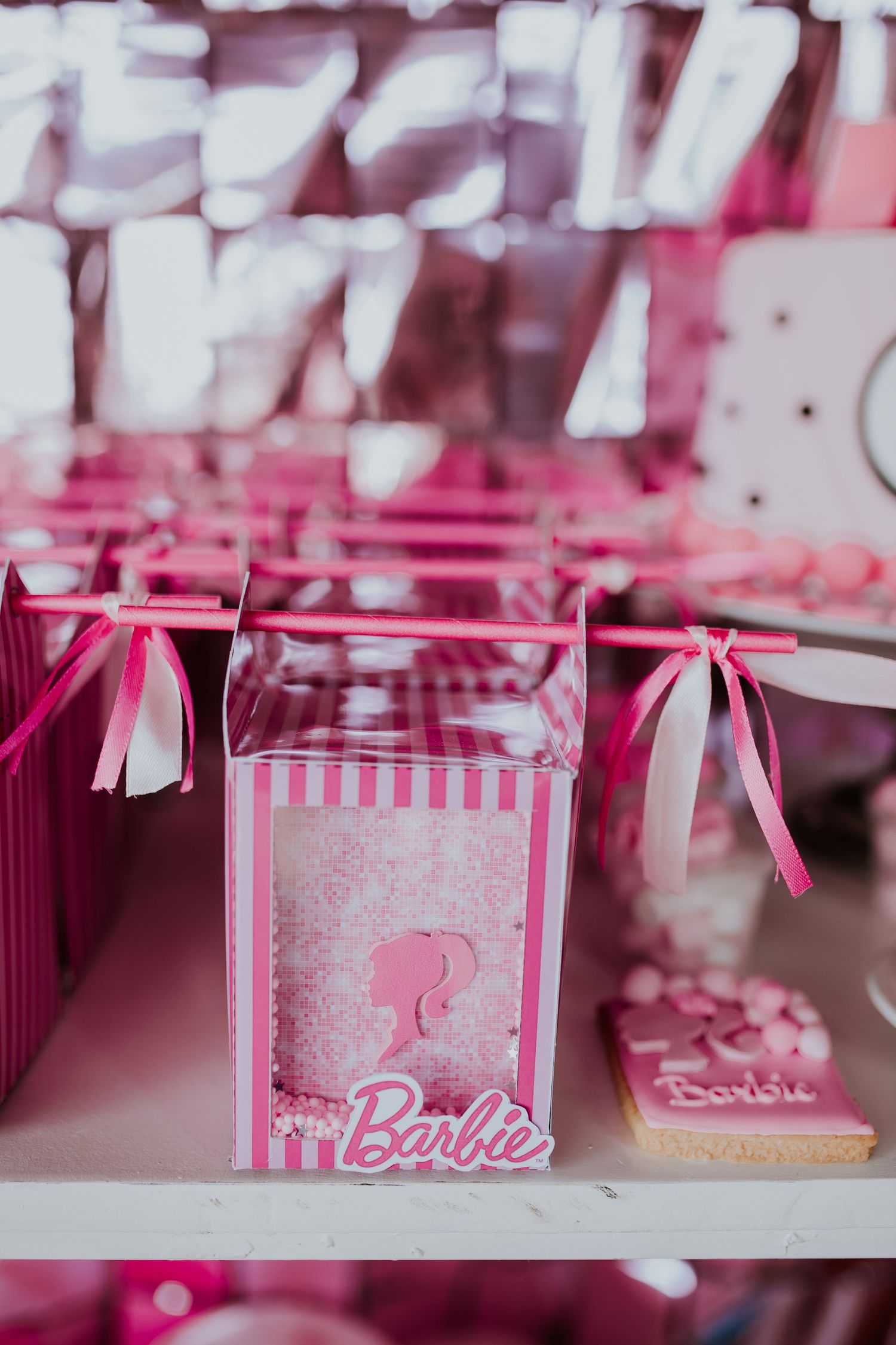 Pink Barbie-themed party decorations with ribbons and glittery boxes arranged in a row for a celebration event.