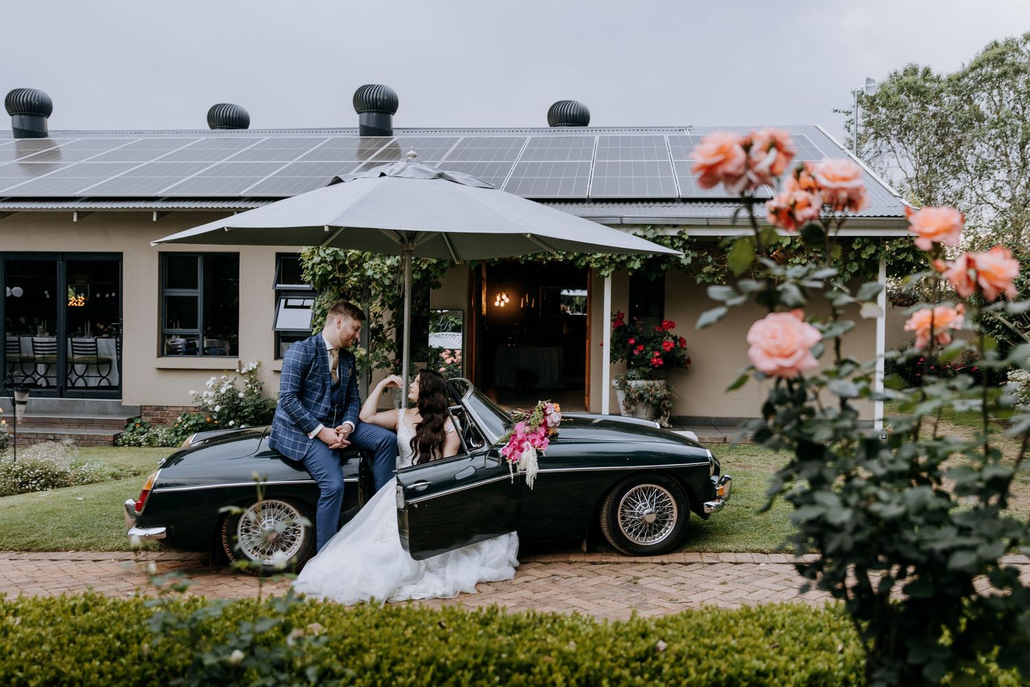 Solar panels installed on a residential rooftop with landscaping and classic car visible in the driveway.