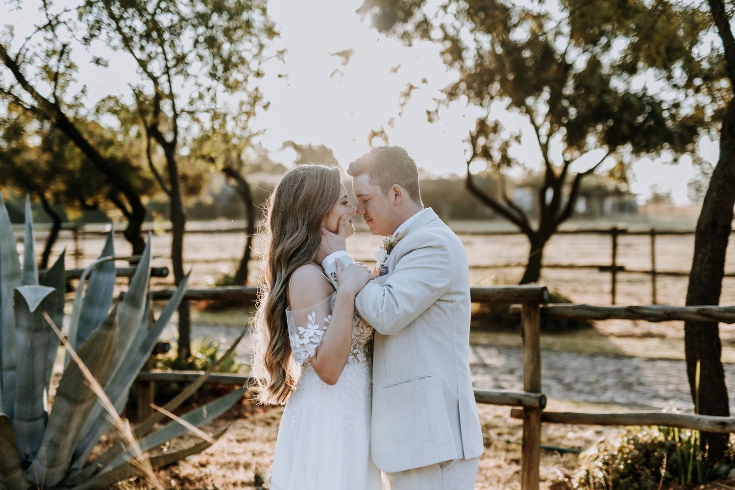 A couple shares an intimate moment in a sunlit outdoor setting with trees and natural scenery in the background.