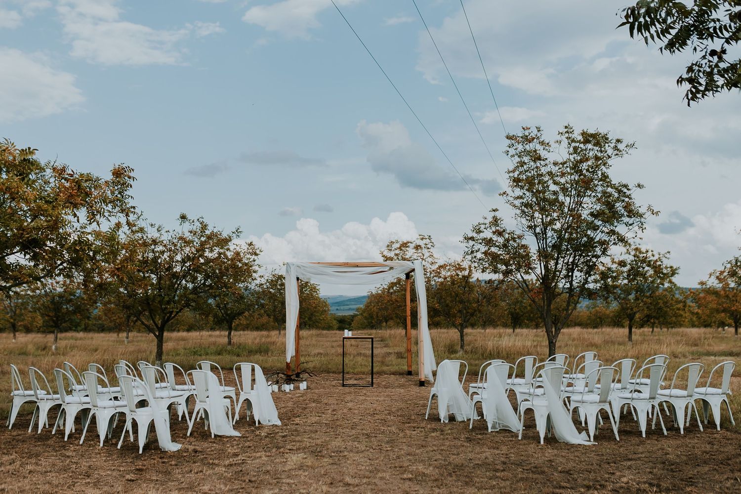 White chairs arranged in curved rows for an outdoor wedding ceremony with trees and fields in the background.