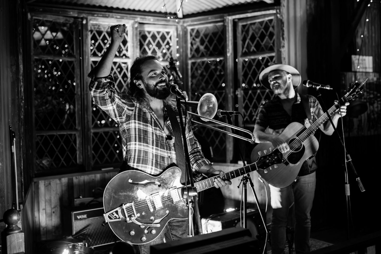 Musicians perform on stage during a live concert with instruments and amplifiers visible in black and white.