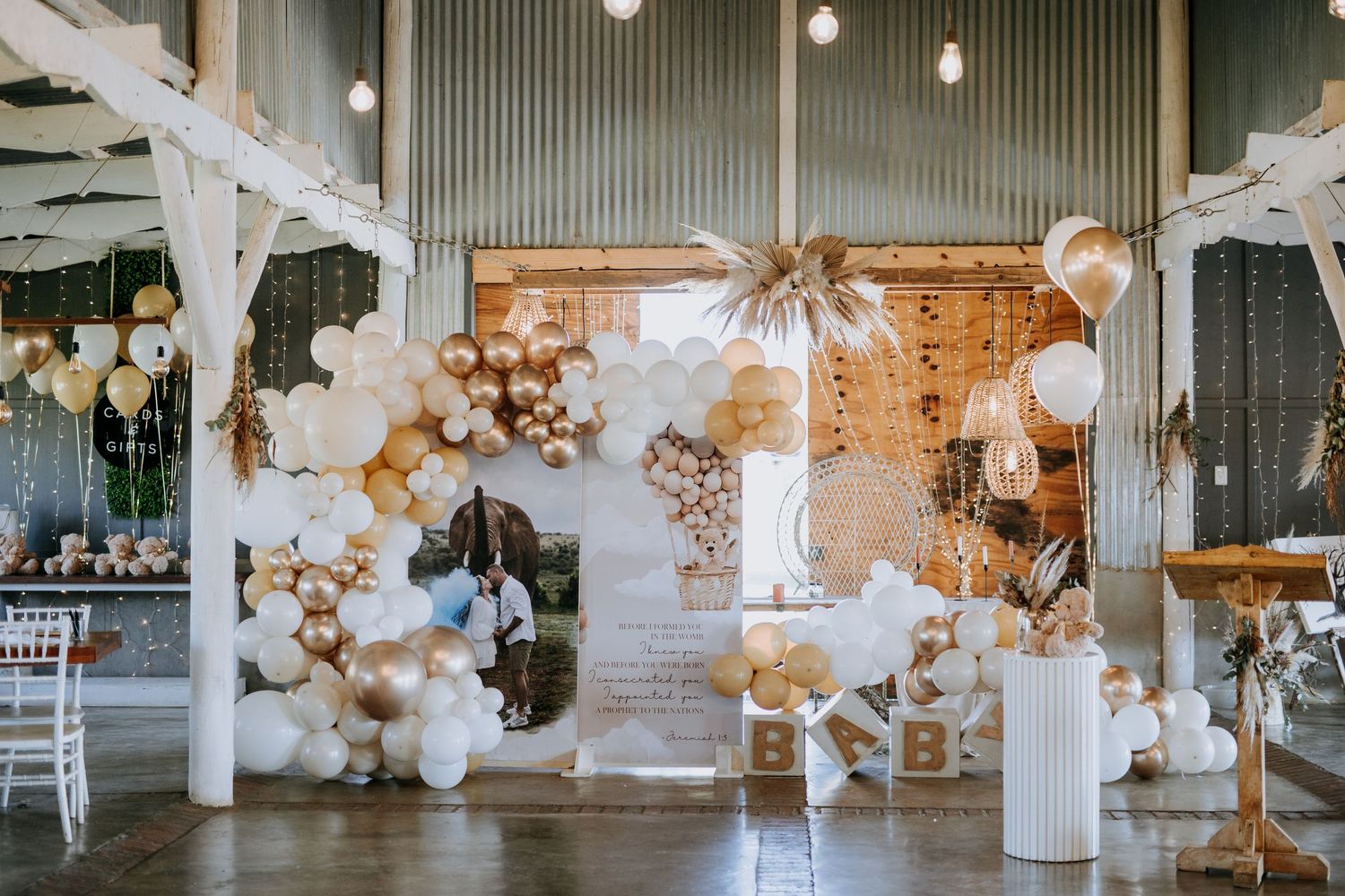 Elegant white indoor wedding venue decorated with ethereal balloon garlands and floral arrangements in a modern space.