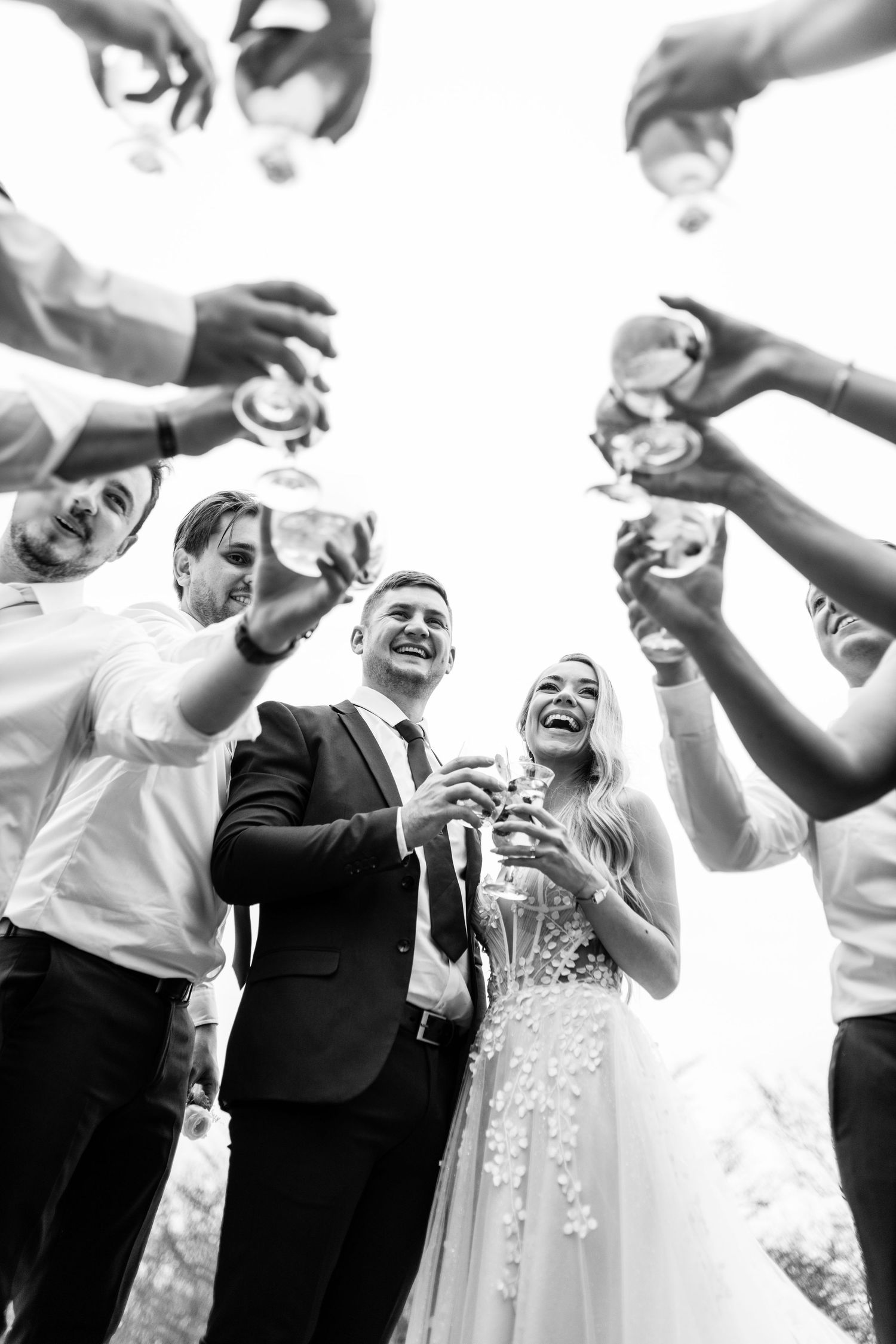 A black and white candid celebratory moment at a wedding reception with guests laughing and raising their hands in joy.