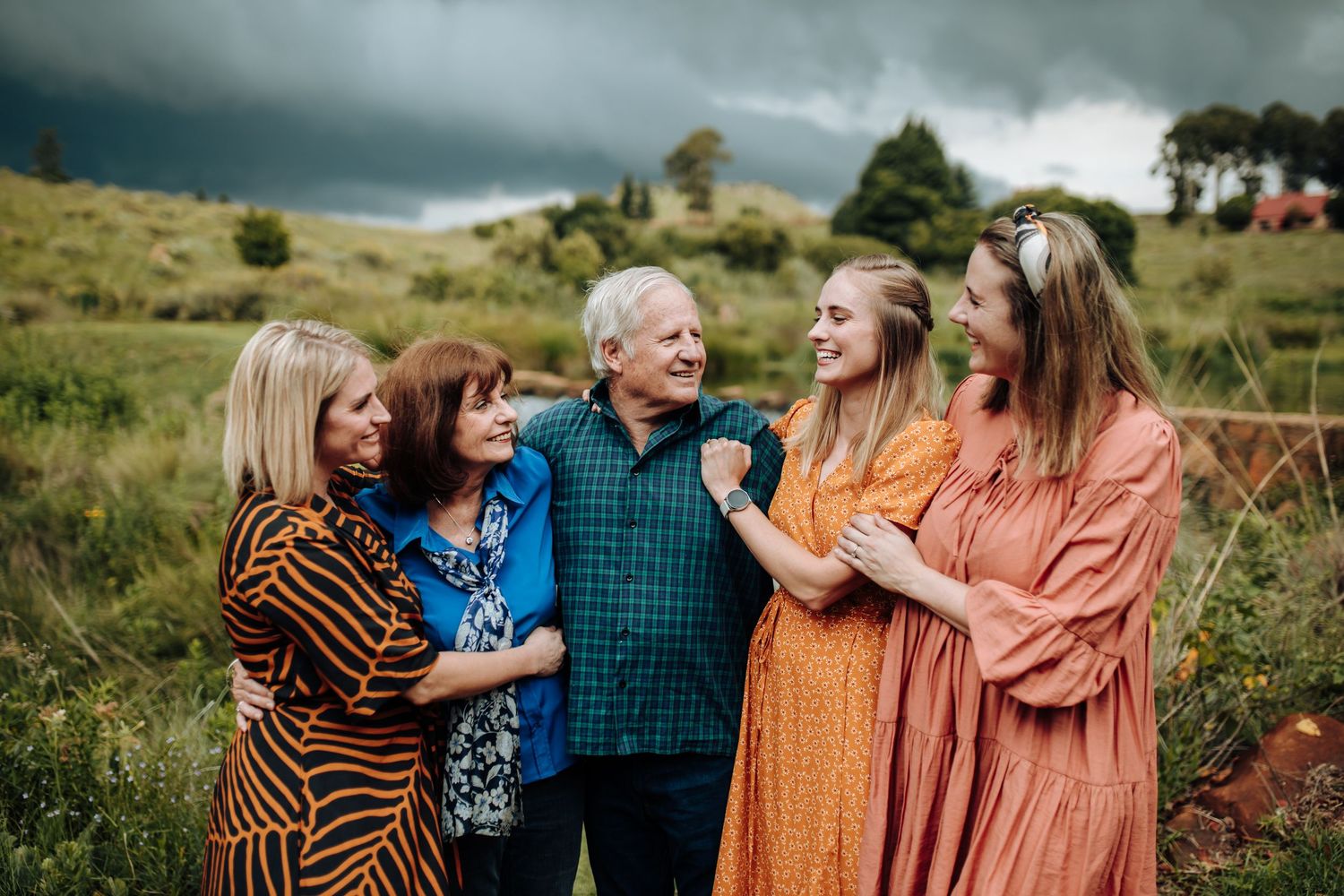 Group shares laughter during an outdoor family photo session in autumn clothing at sunset.