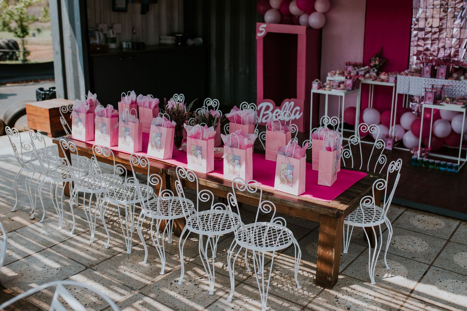 Pink and white chairs line up outside a cafe storefront with colorful dining tables and umbrellas.