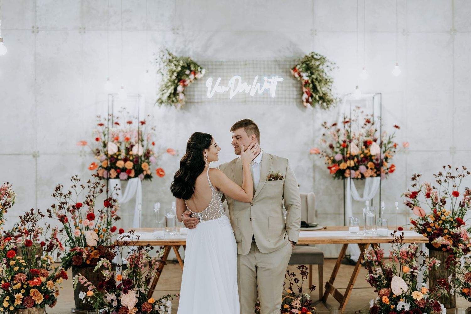 A couple shares an intimate moment during their wedding ceremony in a bright white room with pink floral decorations.