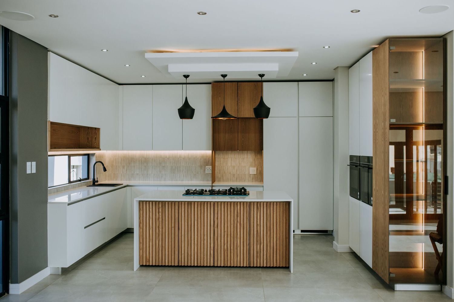 Modern open concept interior with white walls, wooden accents and floor-to-ceiling windows in hallway and kitchen area.