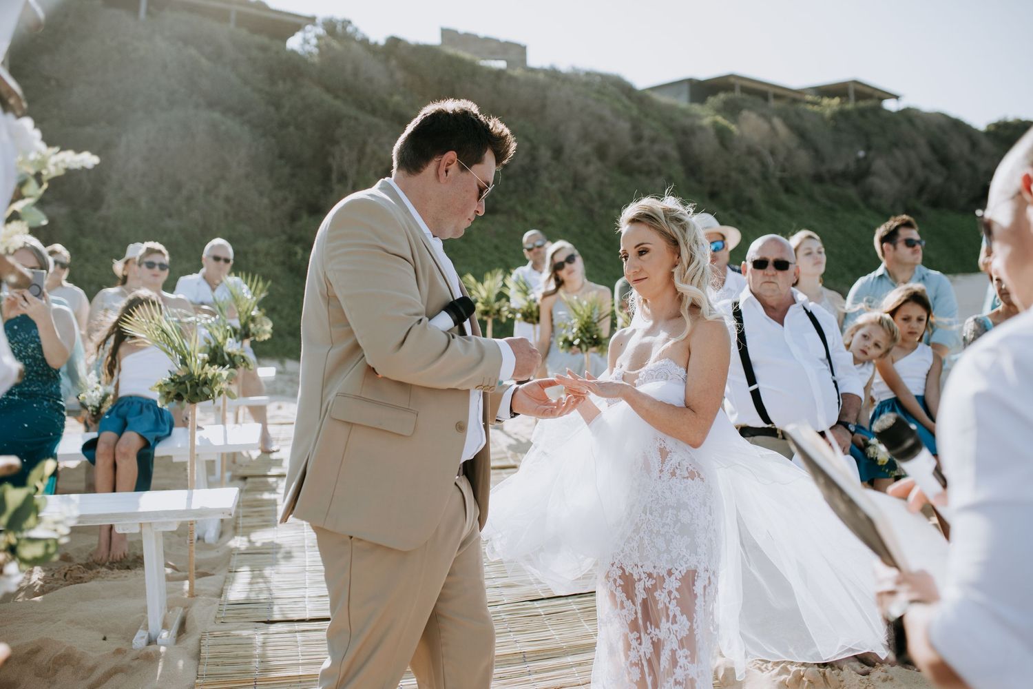 Bride in flowing white dress dancing with guests during an outdoor wedding celebration near the beach.