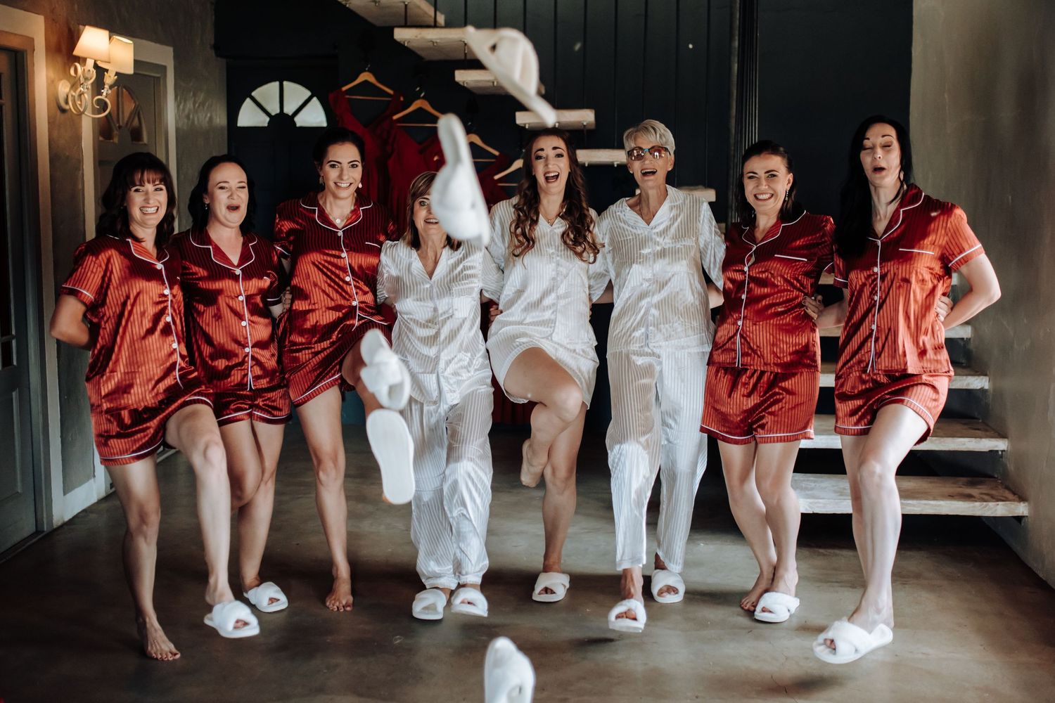 A row of wedding party members in contrasting red and white outfits pose together in a rustic venue.