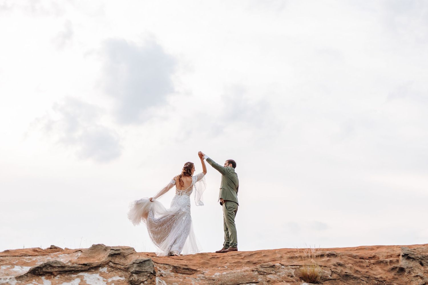 Two figures celebrate together on a scenic desert rock formation under cloudy skies at golden hour.