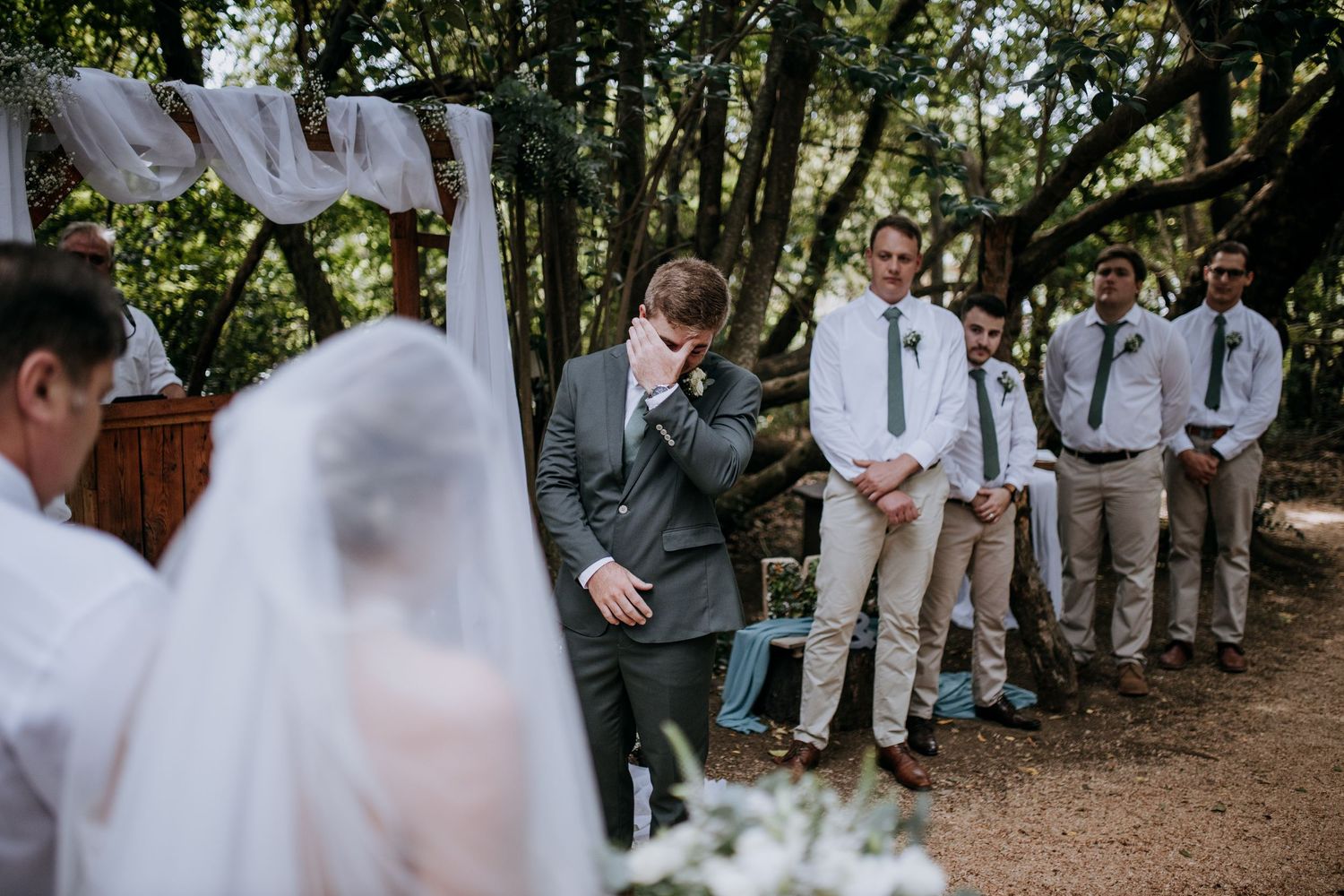 Wedding party stands in a shaded garden path surrounded by lush greenery at an outdoor celebration.