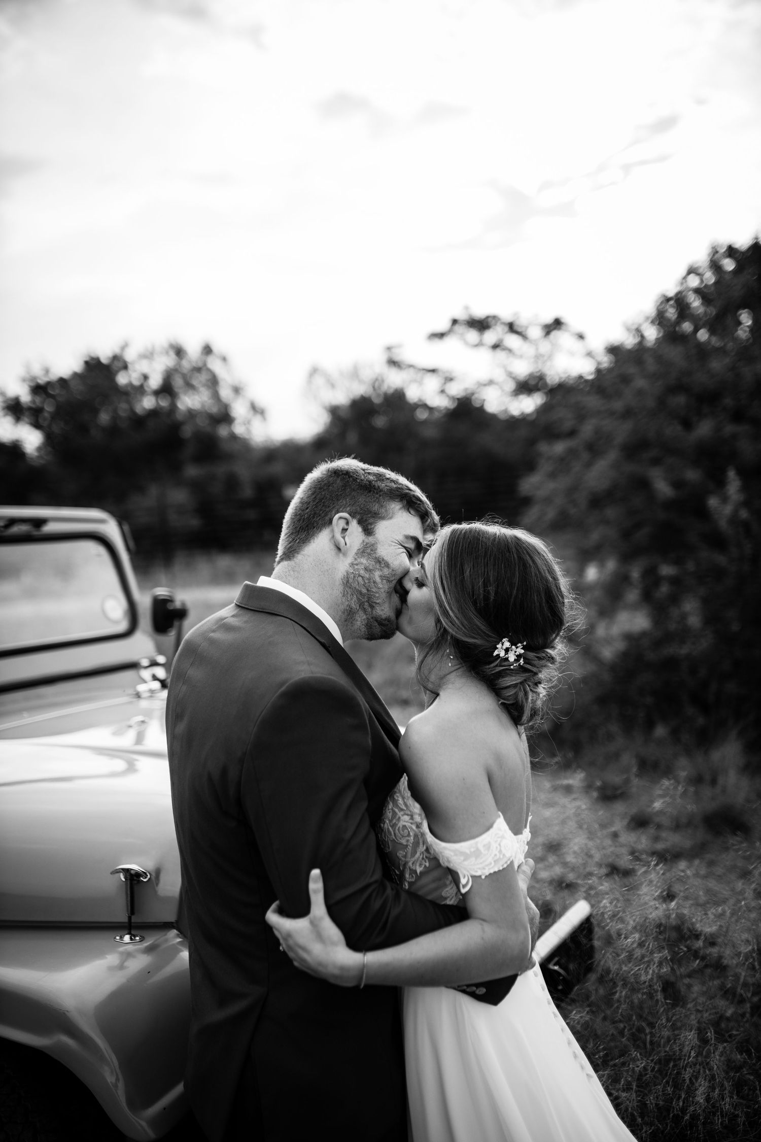 A romantic black and white photo series featuring a couple sharing intimate moments by a vintage car.