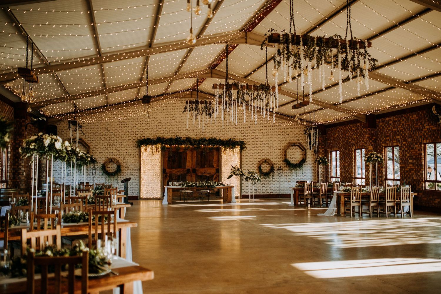 A rustic barn venue interior with exposed wood beams and elegant crystal chandeliers creates a romantic wedding reception space.