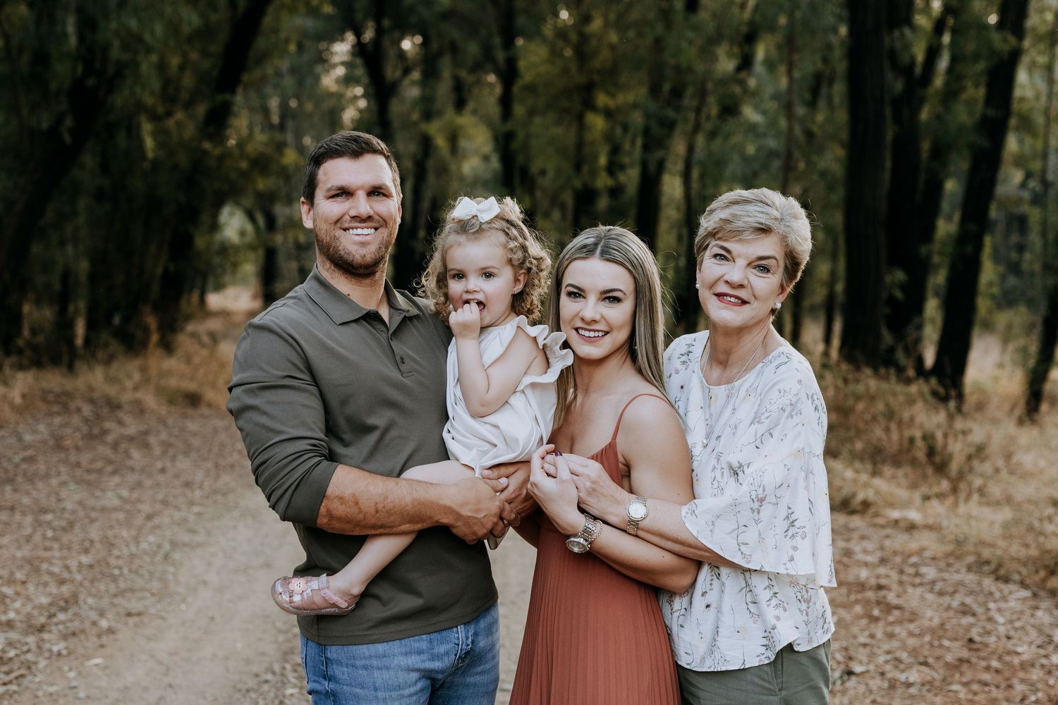 A loving family sits together on fallen autumn leaves during an outdoor portrait session in a wooded area.